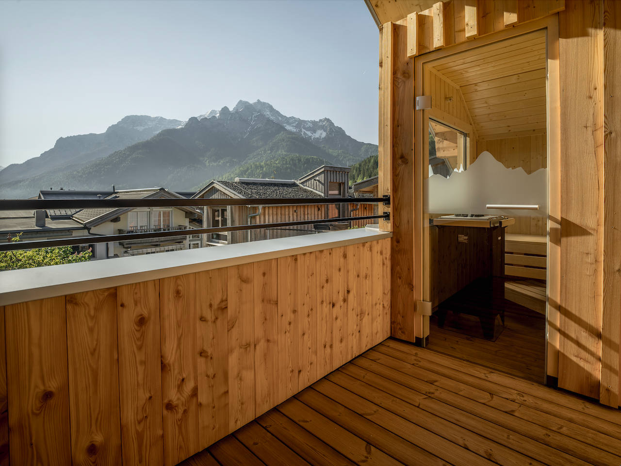 A modern wooden balcony with a view of the mountains. The sun shines on the surroundings, creating a relaxing atmosphere.