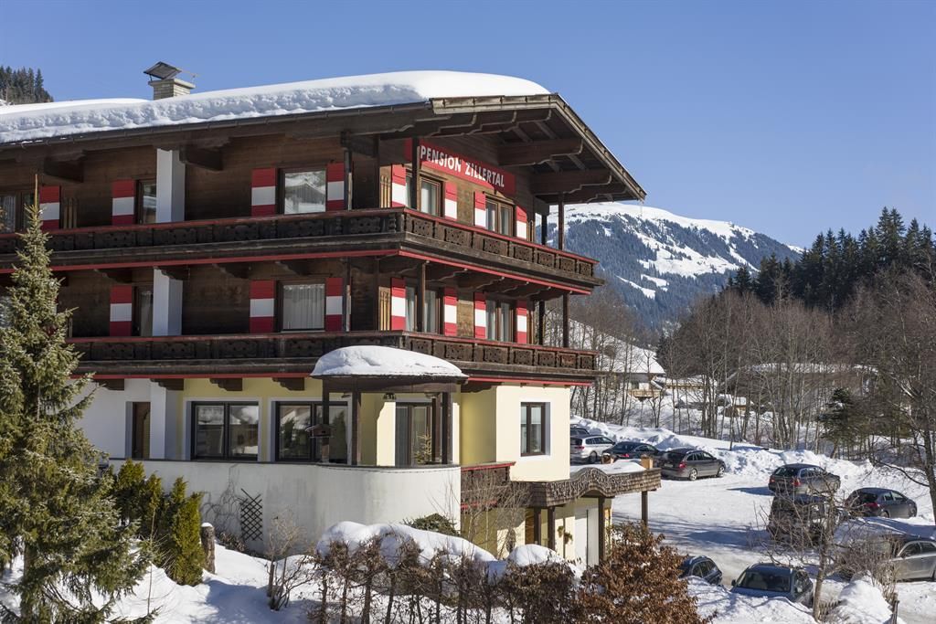 A cozy hotel in the snowy mountains, surrounded by fir trees. The clear winter air and the mountains in the background create an inviting atmosphere.