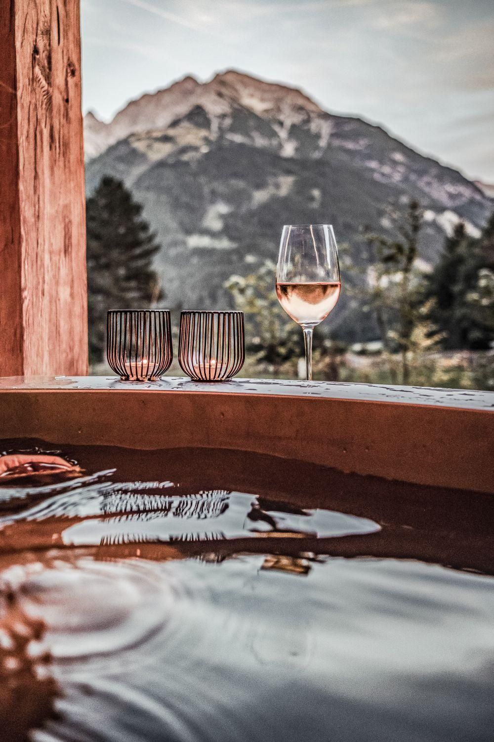 A relaxing bath in the hot pot with a view of the mountains. On the edge, there are wine glasses and a calm atmosphere is palpable.