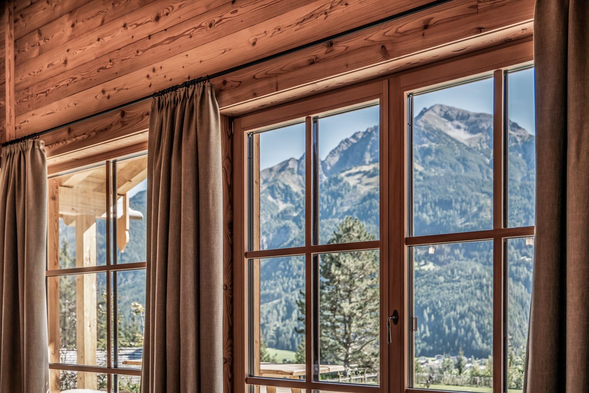 A cozy room with wood paneling and large windows. The view extends to impressive mountains and forested areas.