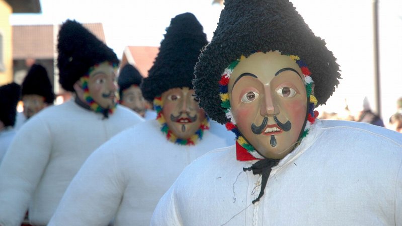 Young men wearing black hats, latticed masks and white shirts, padded out with hay, parade across the village of Axams, © Fasnachtsverein Axams