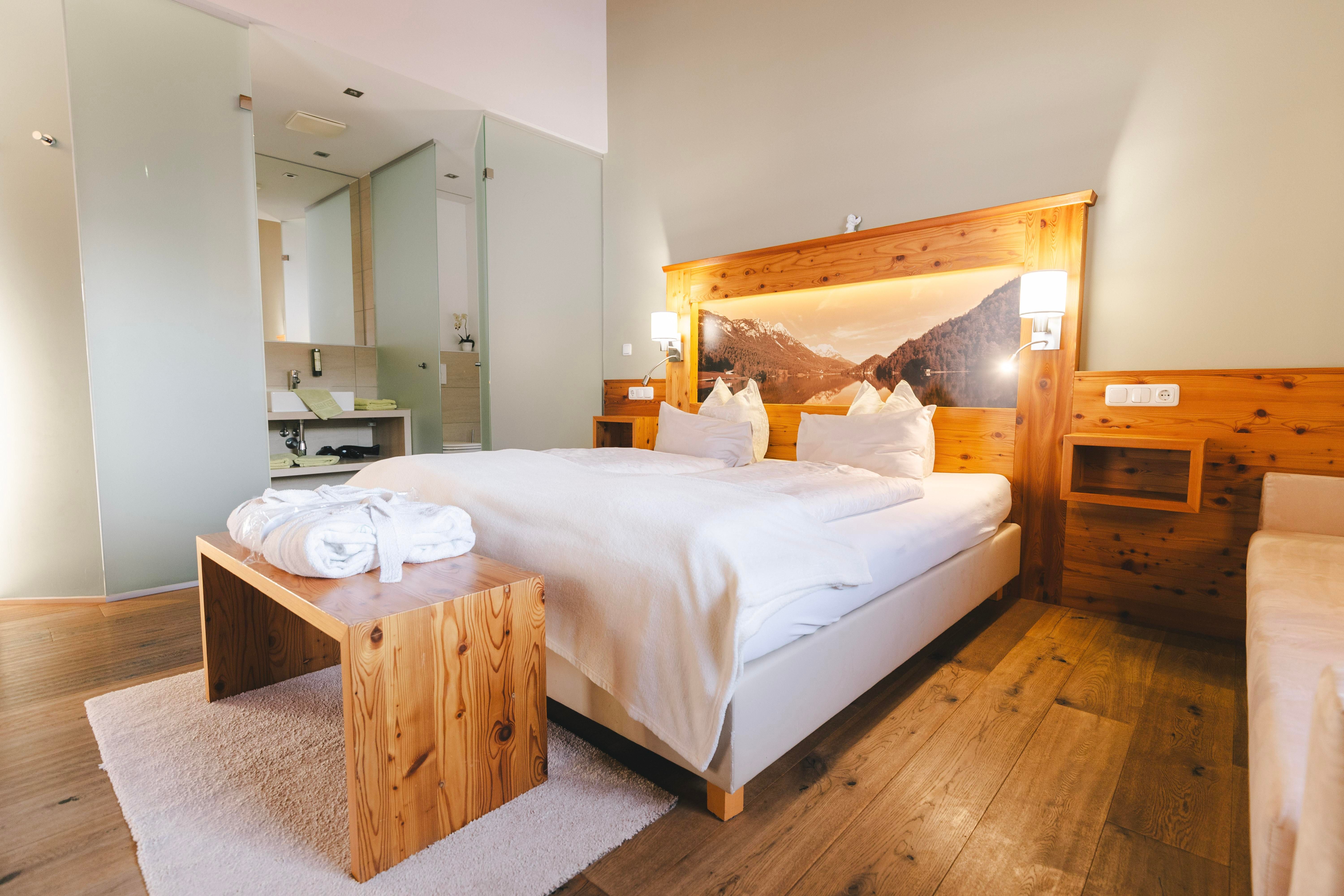 A cozy room with a large bed and wooden details. The bright ambiance creates a relaxing atmosphere.