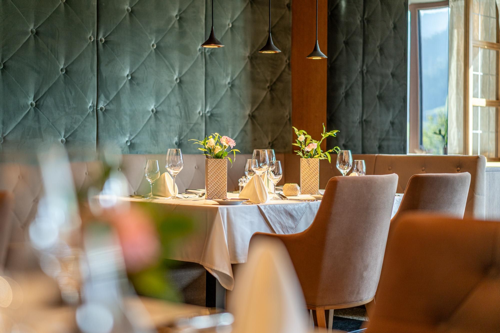 An elegant dining area with beautifully set tables. The walls are painted in a rich green, and small floral arrangements beautify the tables.