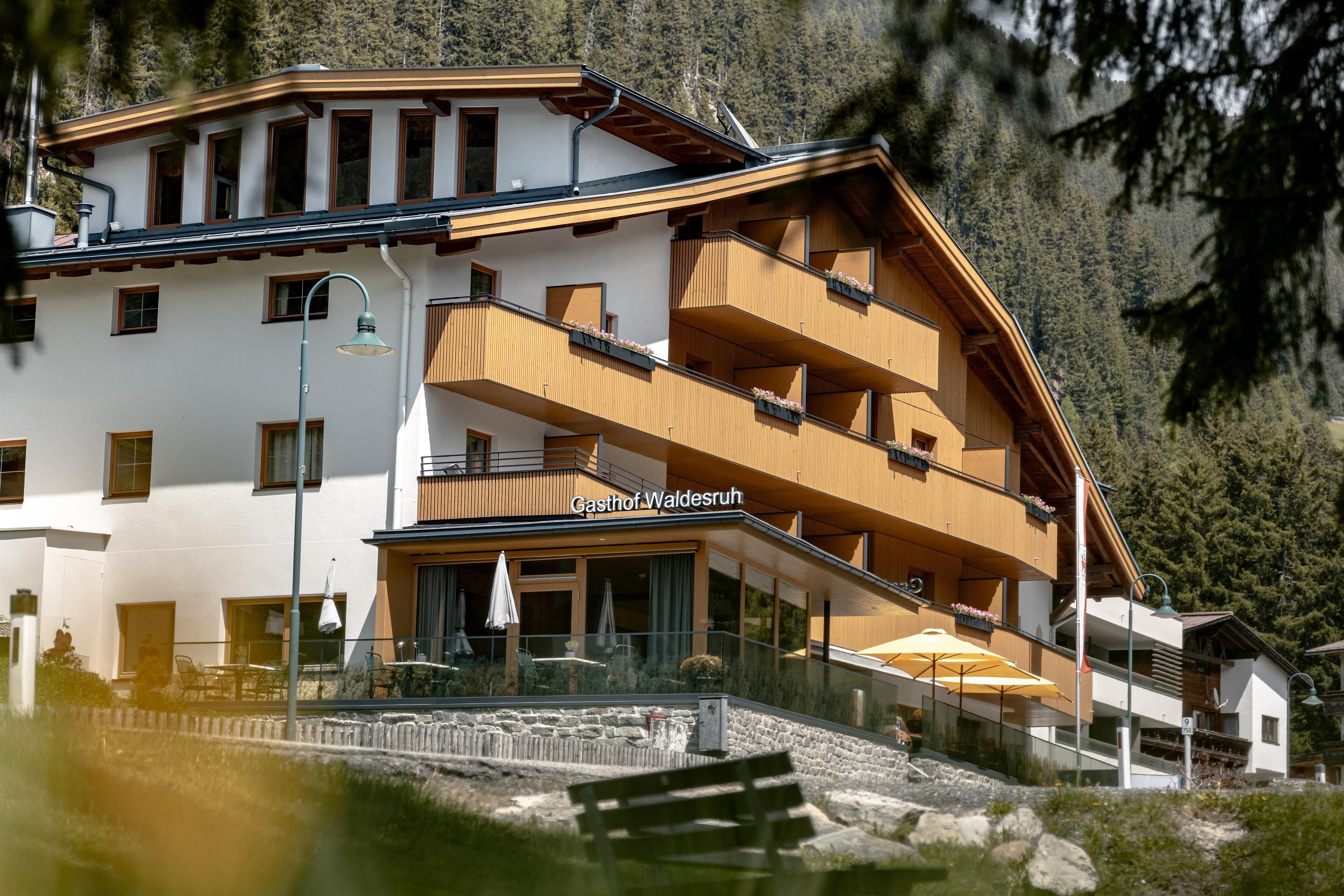 A modern hotel with wooden cladding and large balconies. It is located in a picturesque mountain landscape.