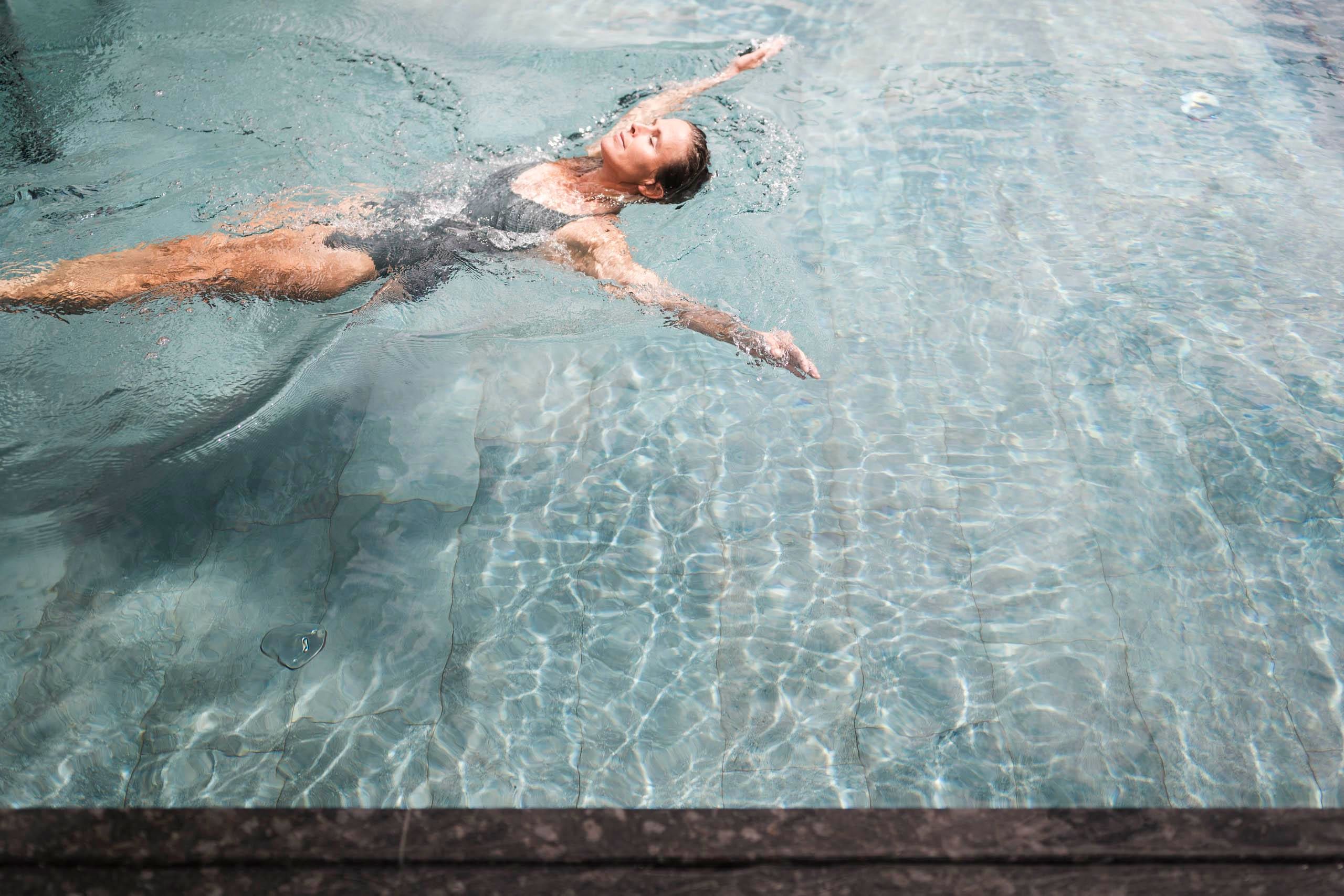 A woman swims relaxed in a clear pool. The water gently reflects the light and creates a calm atmosphere.