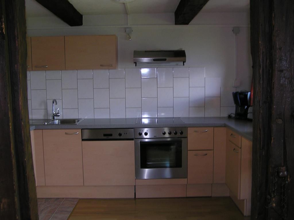 A modern kitchen with wooden furniture and bright tiles. It includes a stove, sink, and kitchen appliances.