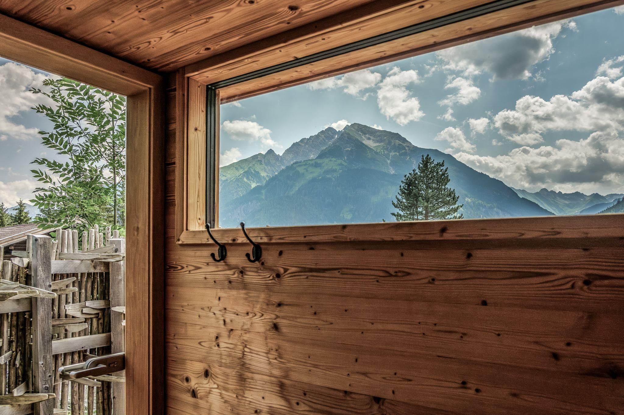 A view from a sauna overlooking majestic mountains and a cloudy sky. Nature is peaceful and inviting.