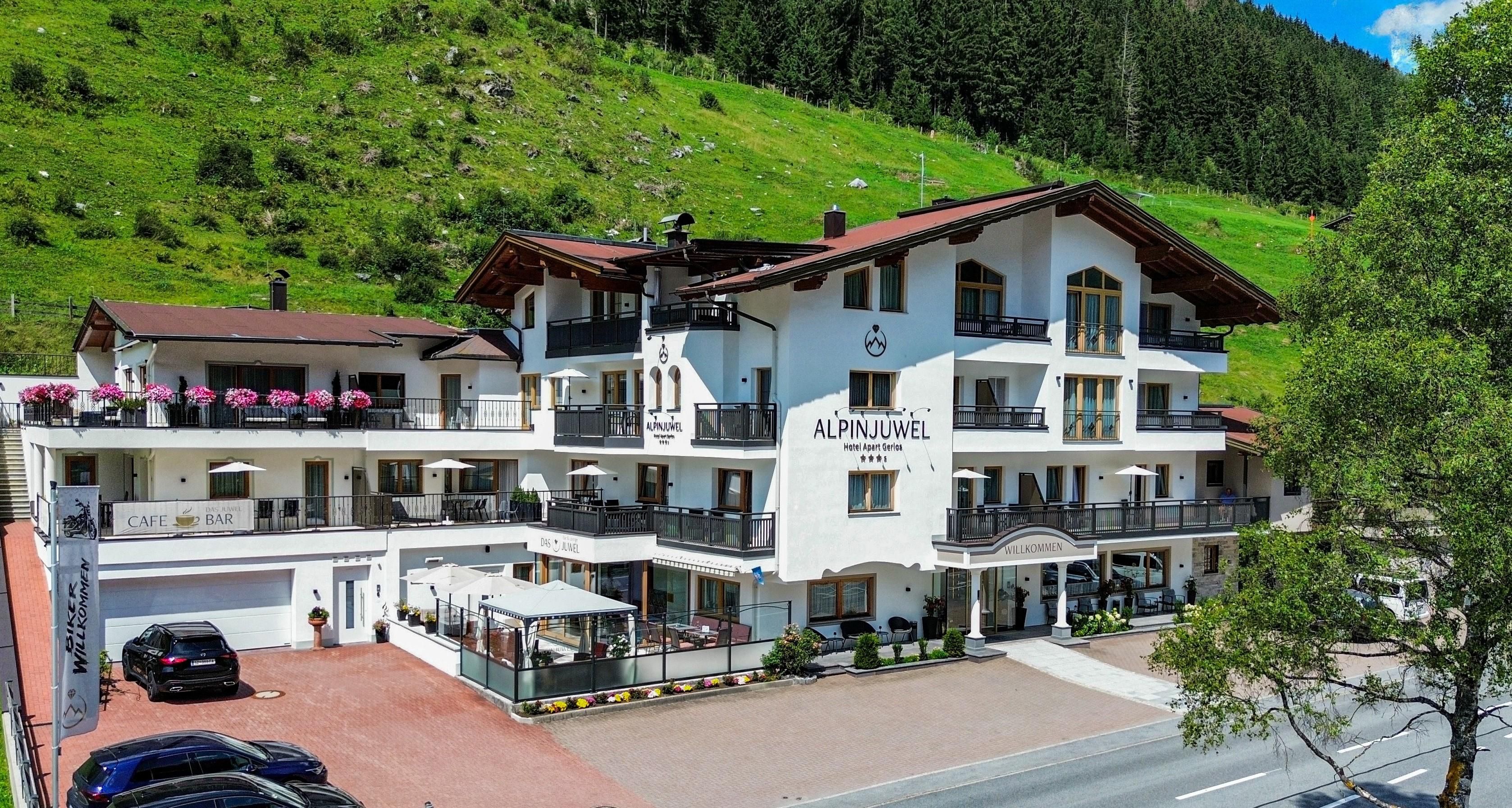 A beautiful hotel with alpine view and green backdrop. It has an inviting terrace and a parking lot located above the street.