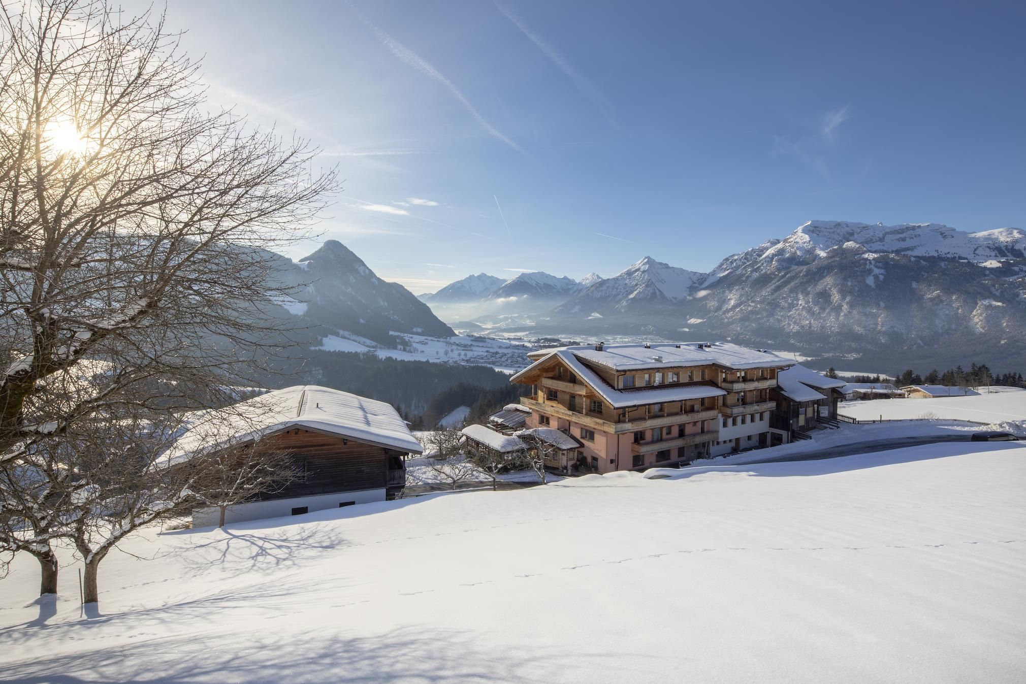 A wintry landscape with snow-covered hills and cottages. In the background, majestic mountains and a clear sky can be seen.
