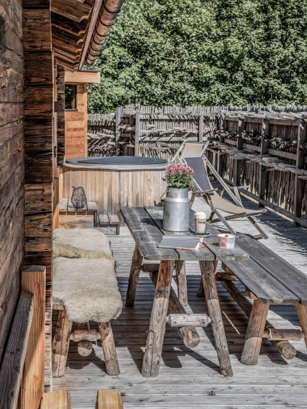 A cozy terrace with rustic wooden furniture and a wooden bathtub. The surroundings are green and invite relaxation.