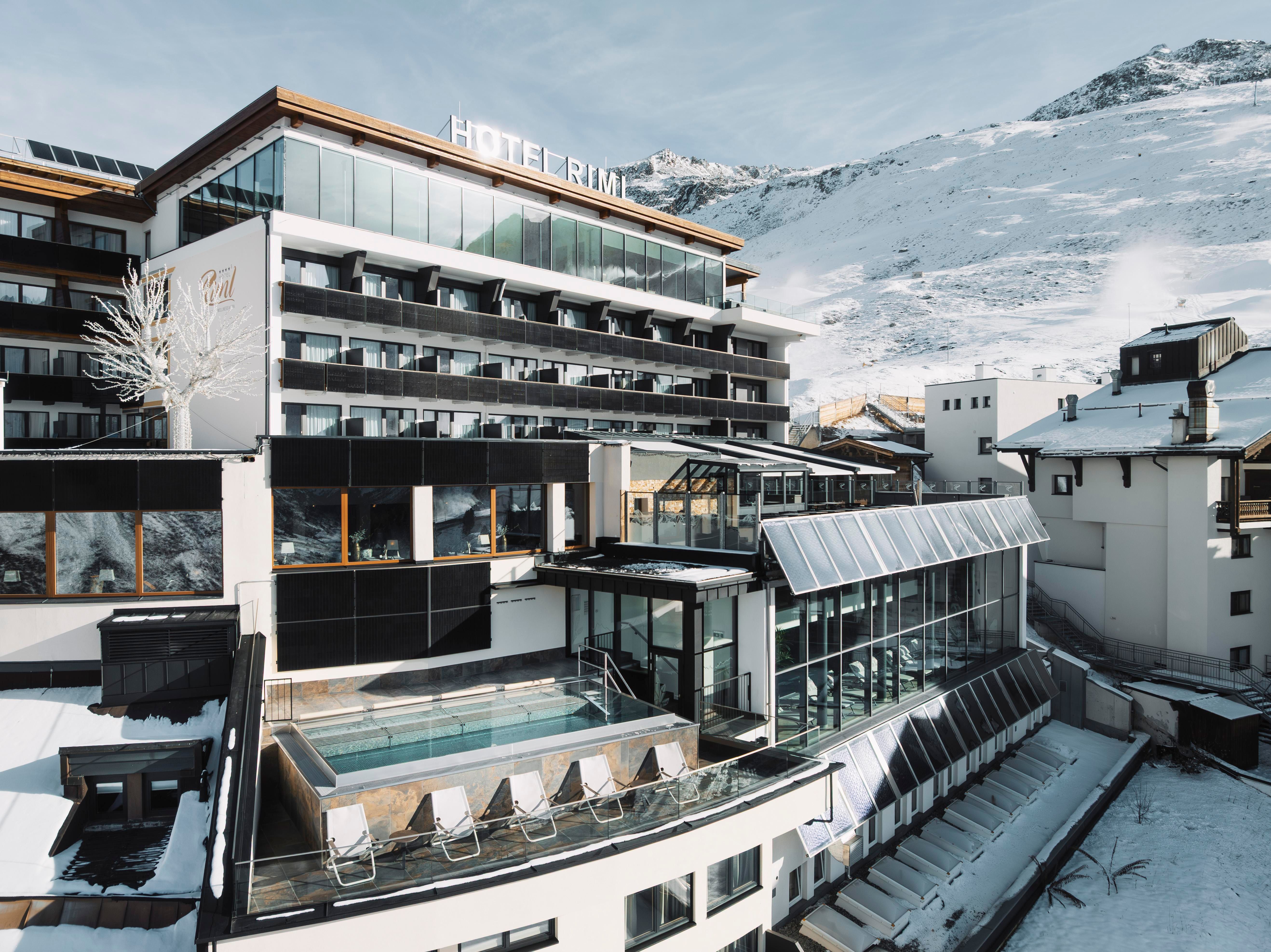 A modern hotel with large windows and a relaxing outdoor swimming pool. The surroundings are covered in snow and offer an impressive mountain view.