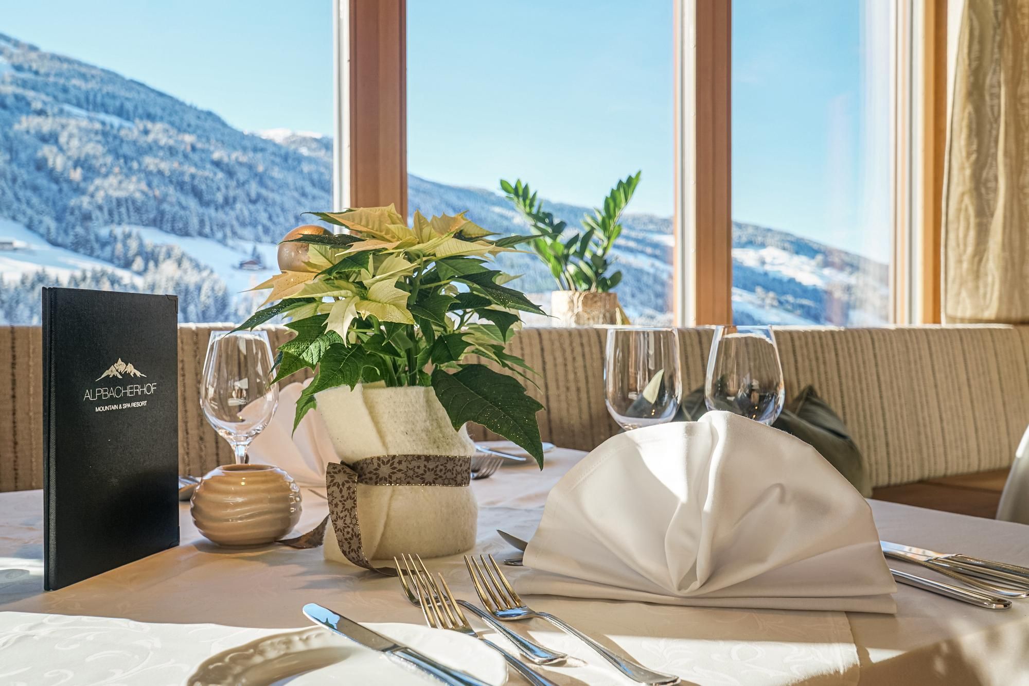 An elegantly set table in the restaurant with a view of snow-covered mountains. The table is arranged with plants, glasses, and cutlery.