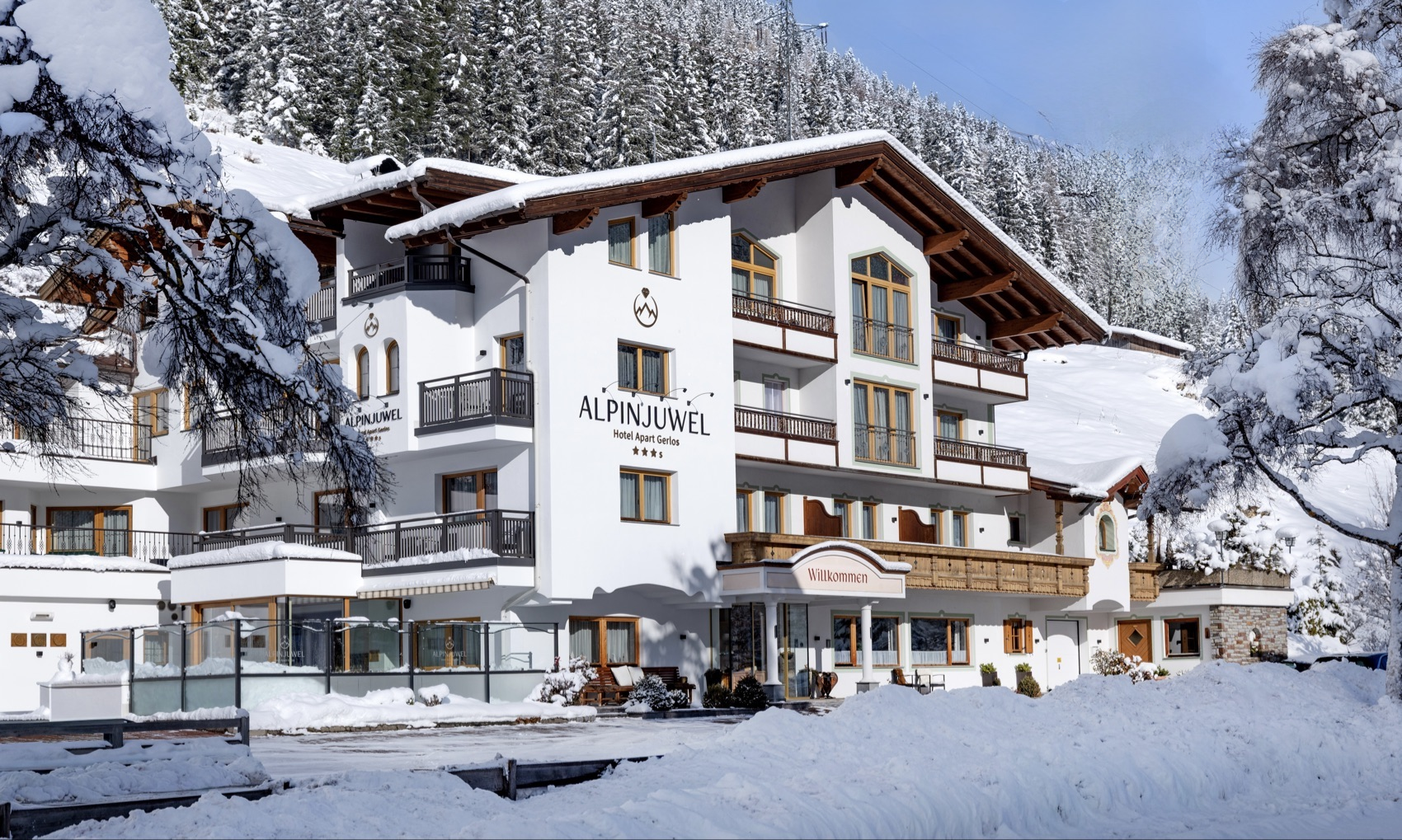 A charming hotel in winter with snow-covered grounds. Surrounded by tall trees and an idyllic mountain landscape.