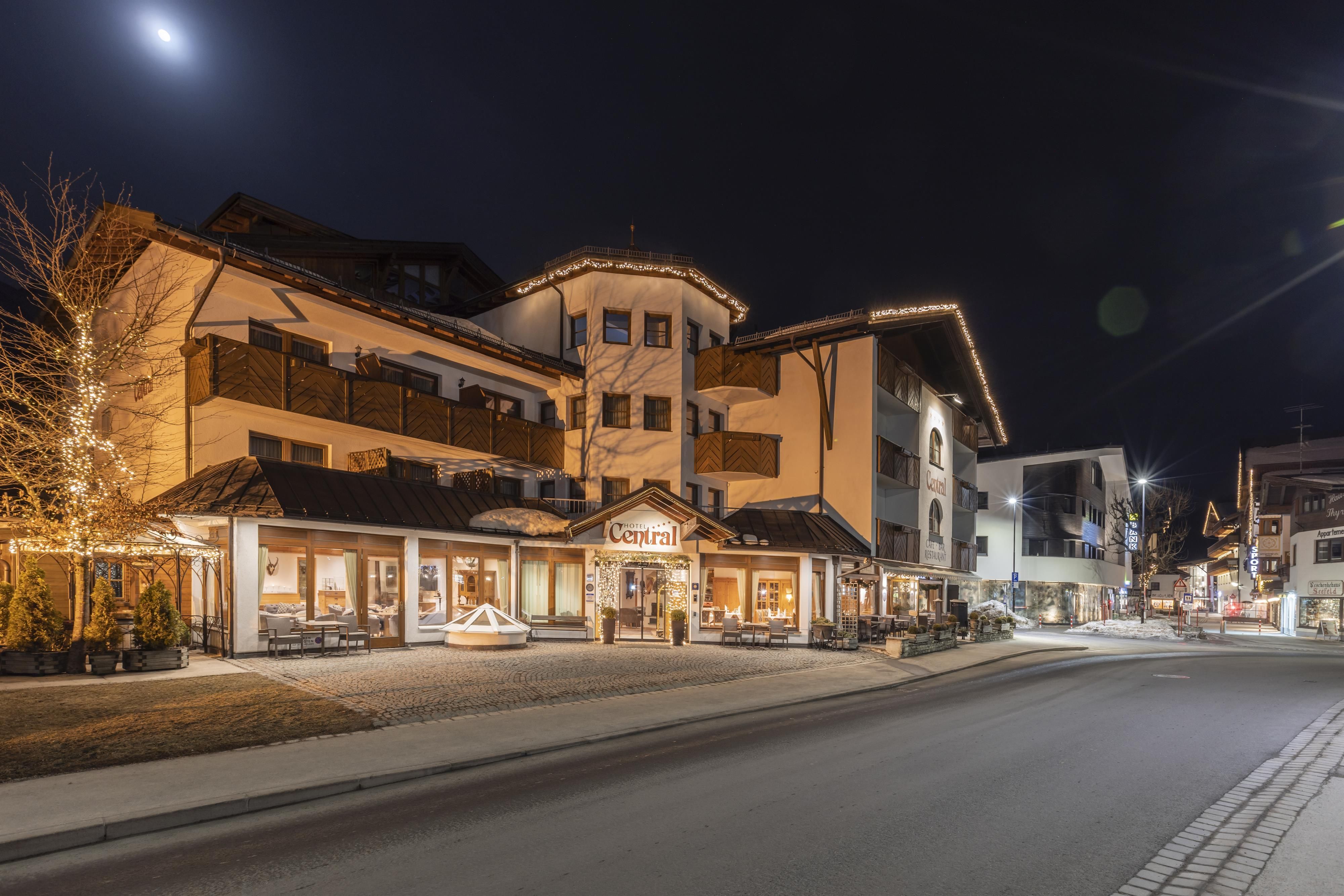 A charming hotel with festive lighting at night. The street is quiet and inviting, surrounded by modern buildings.