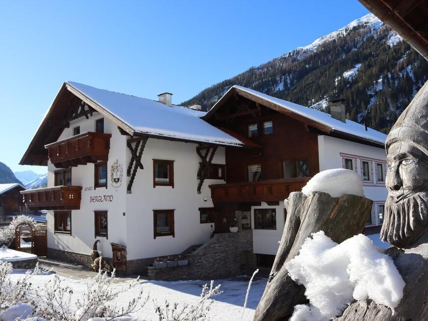 An idyllic house in the snow with traditional architecture. In the background, snow-covered mountains and a blue sky are visible.