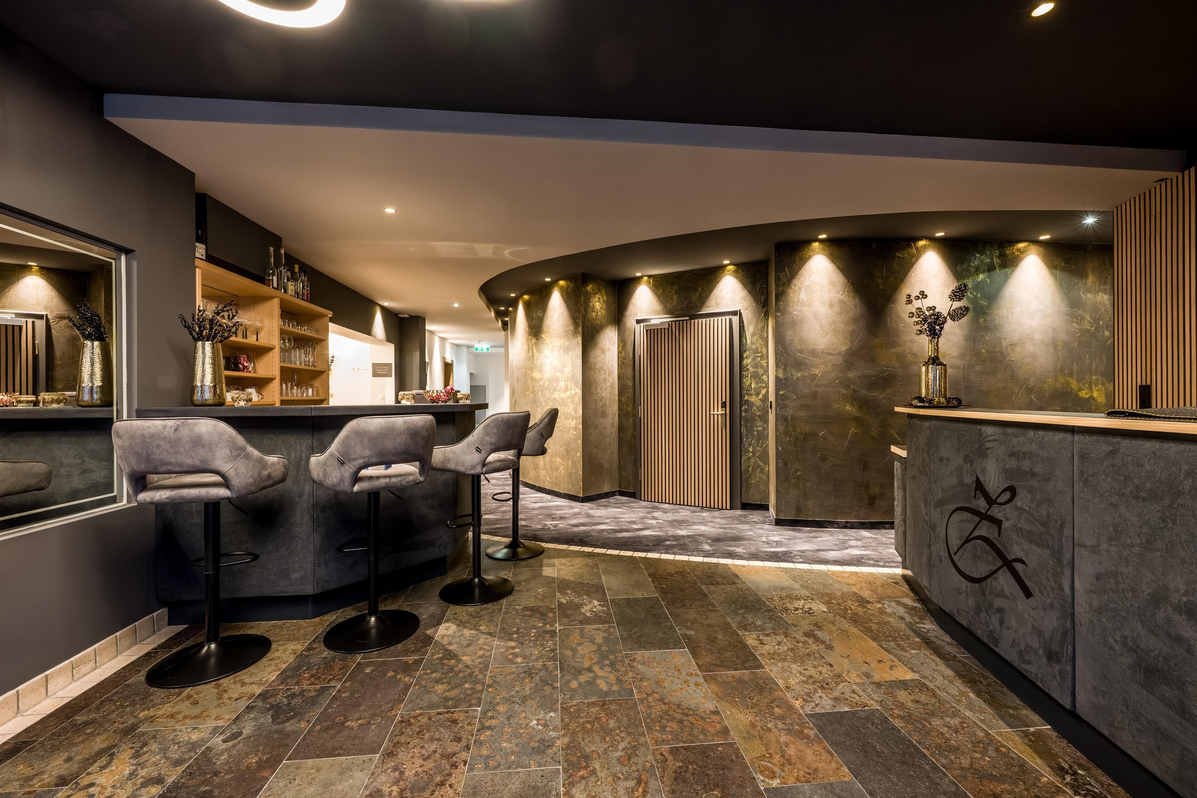 An elegant reception hall with a modern bar area and stylish bar stools. The walls are in muted colors and the lighting creates an inviting atmosphere.