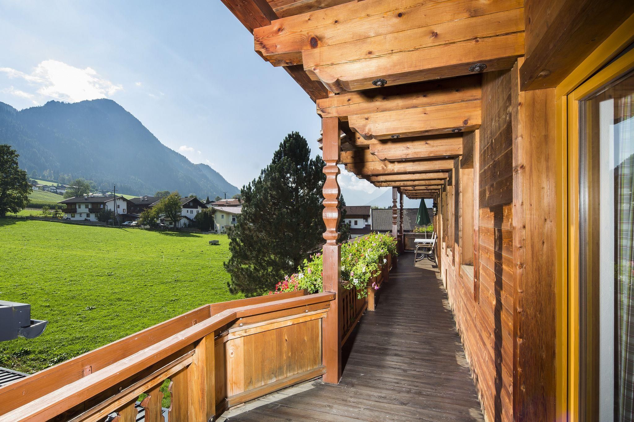 A wooden balcony overlooking green meadows and mountains. The sun is shining and the sky is clear.