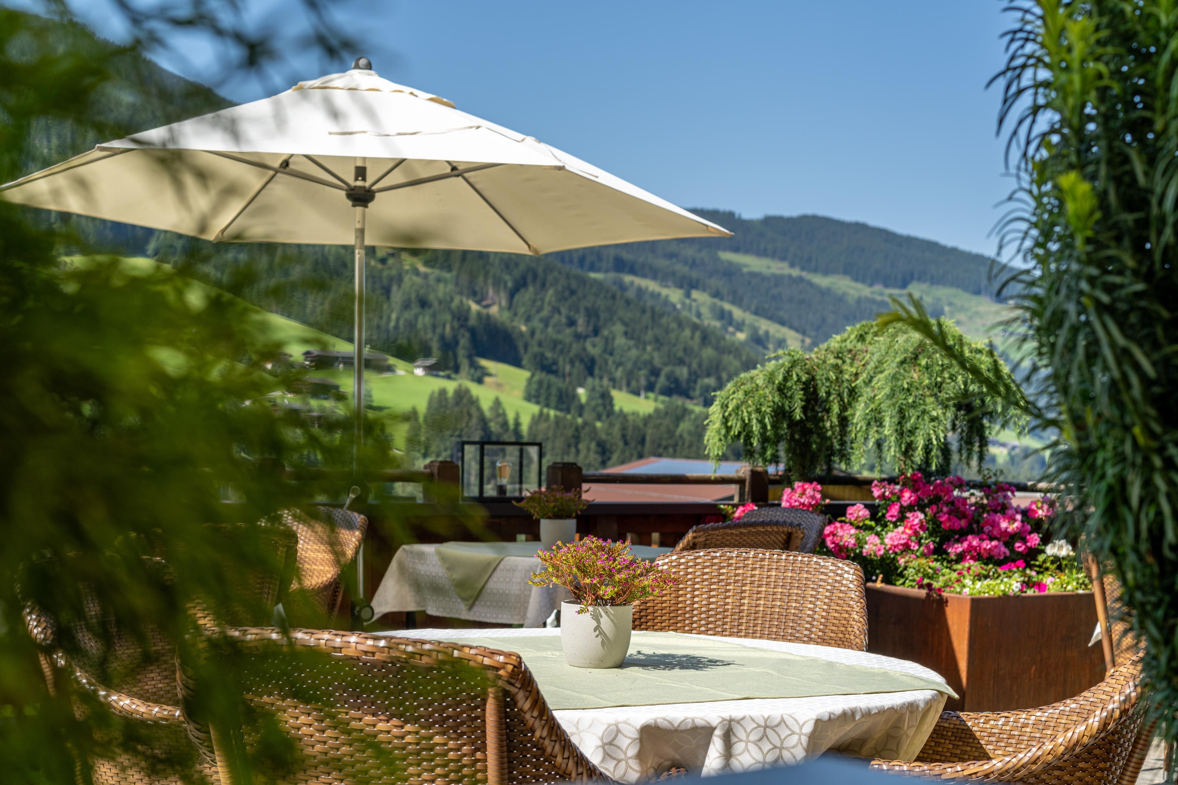 A beautiful outdoor area with rattan furniture and a sun umbrella. Flowers and green landscapes create an inviting atmosphere.