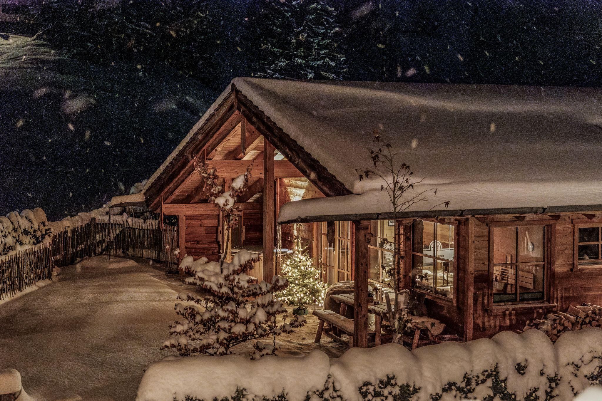 A pretty chalet hidden under a layer of snow. The surroundings are wintery and festively illuminated.