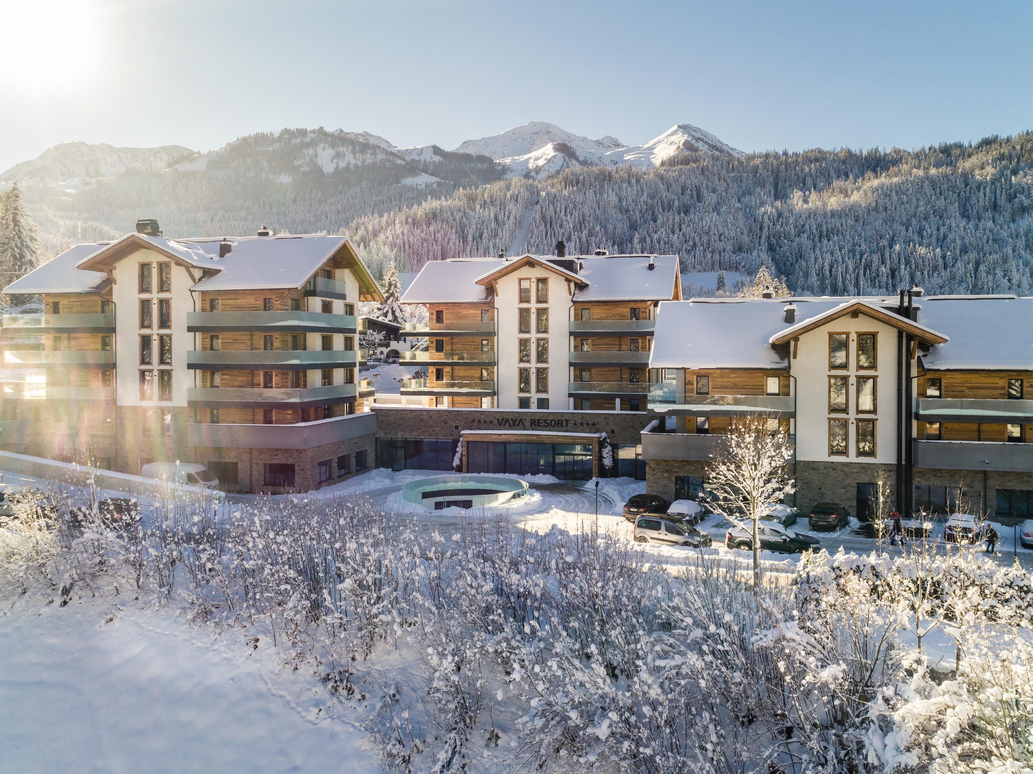 A charming residential complex in the snow, surrounded by mountains. The buildings are designed to be modern and cozy.