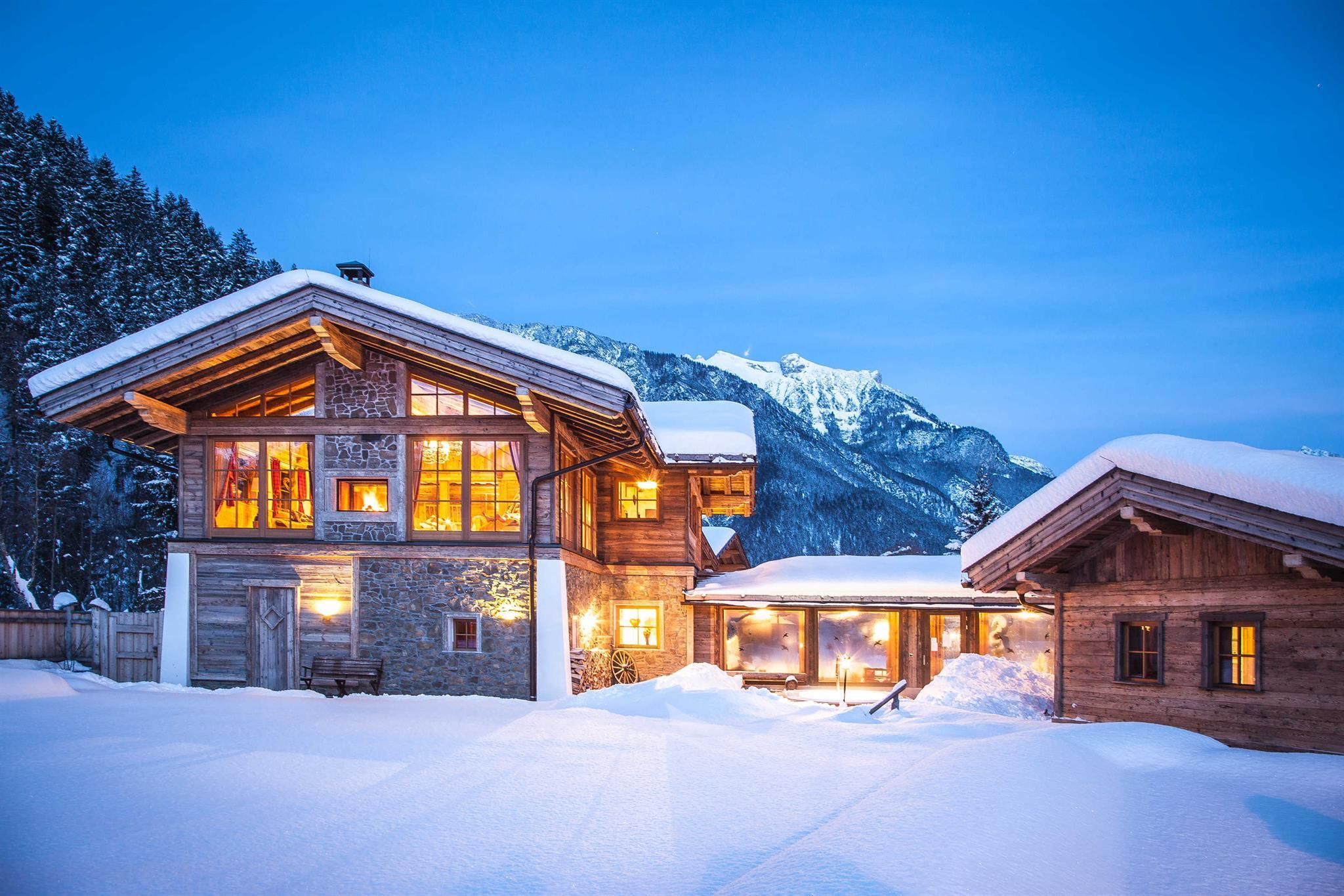 A charming chalet in a snowy landscape. The warm lights reflect in the serene evening setting.