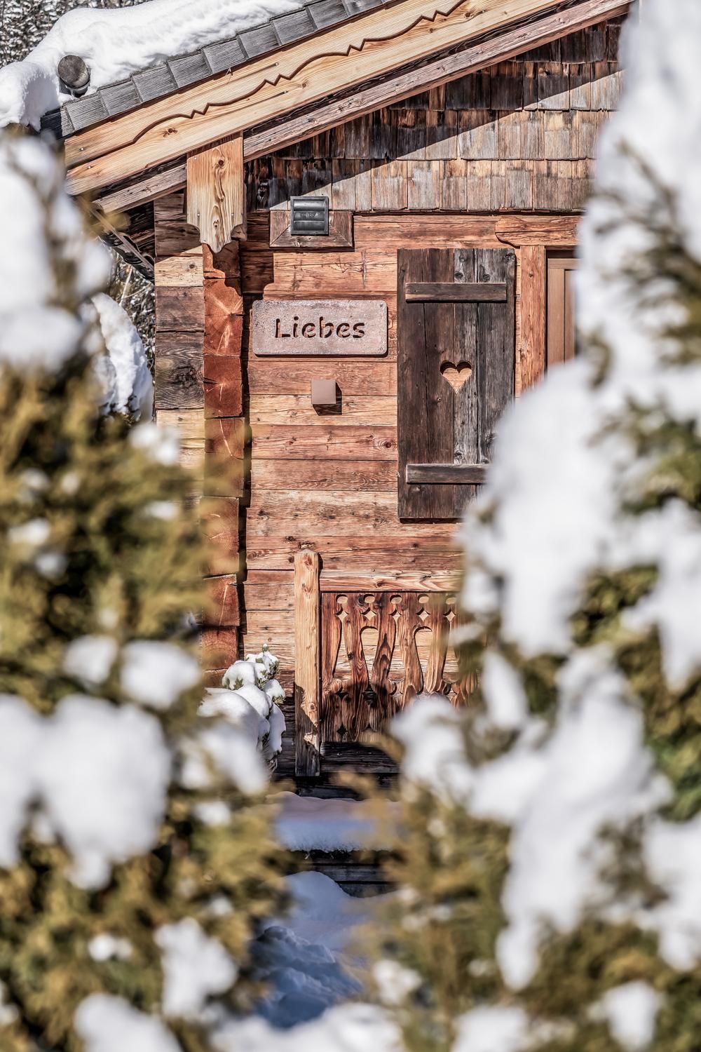 A cozy chalet in the snow with a heart in the window.