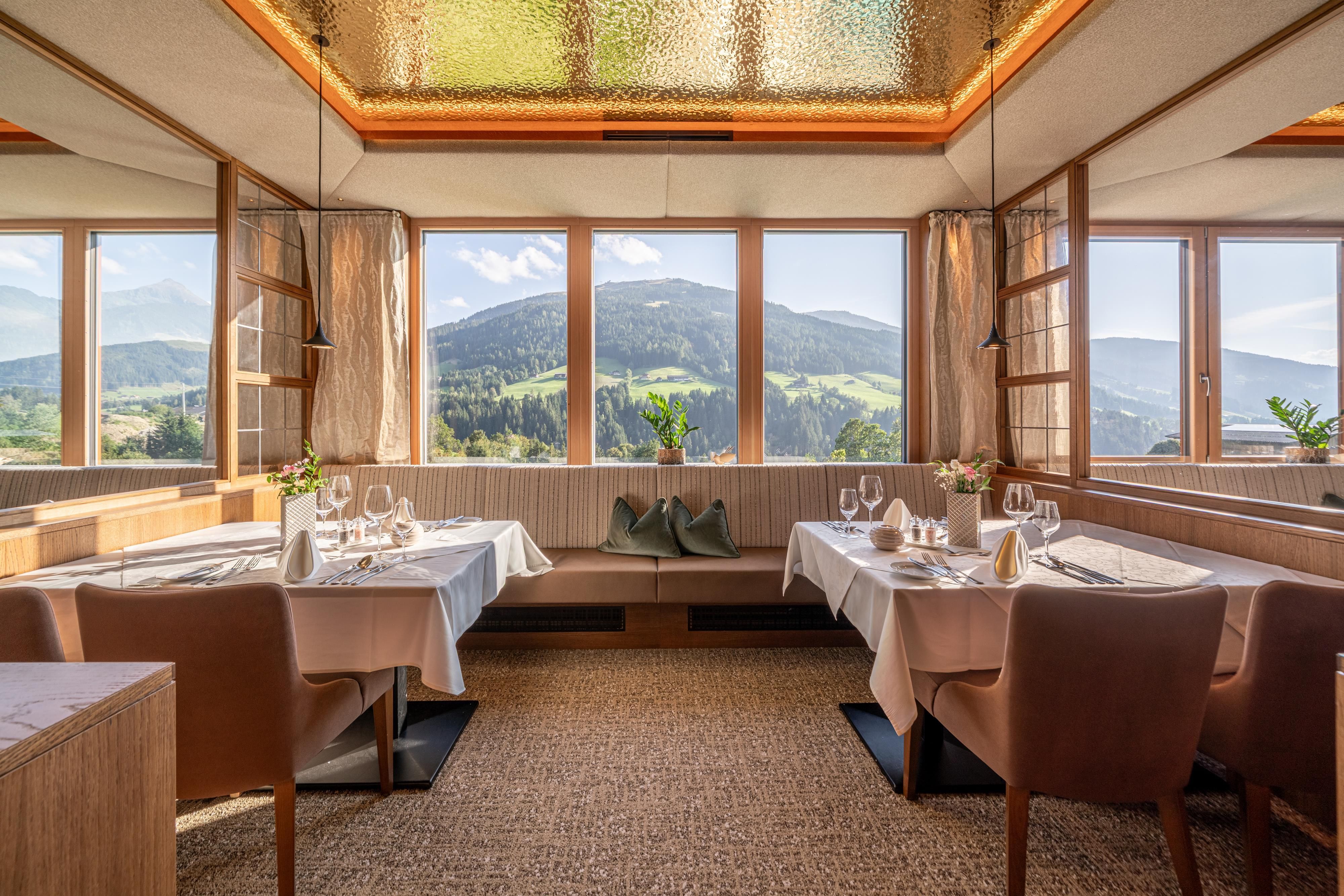 An elegant restaurant with tables that are dressed in white. Large windows provide a view of the mountains and the green landscape.