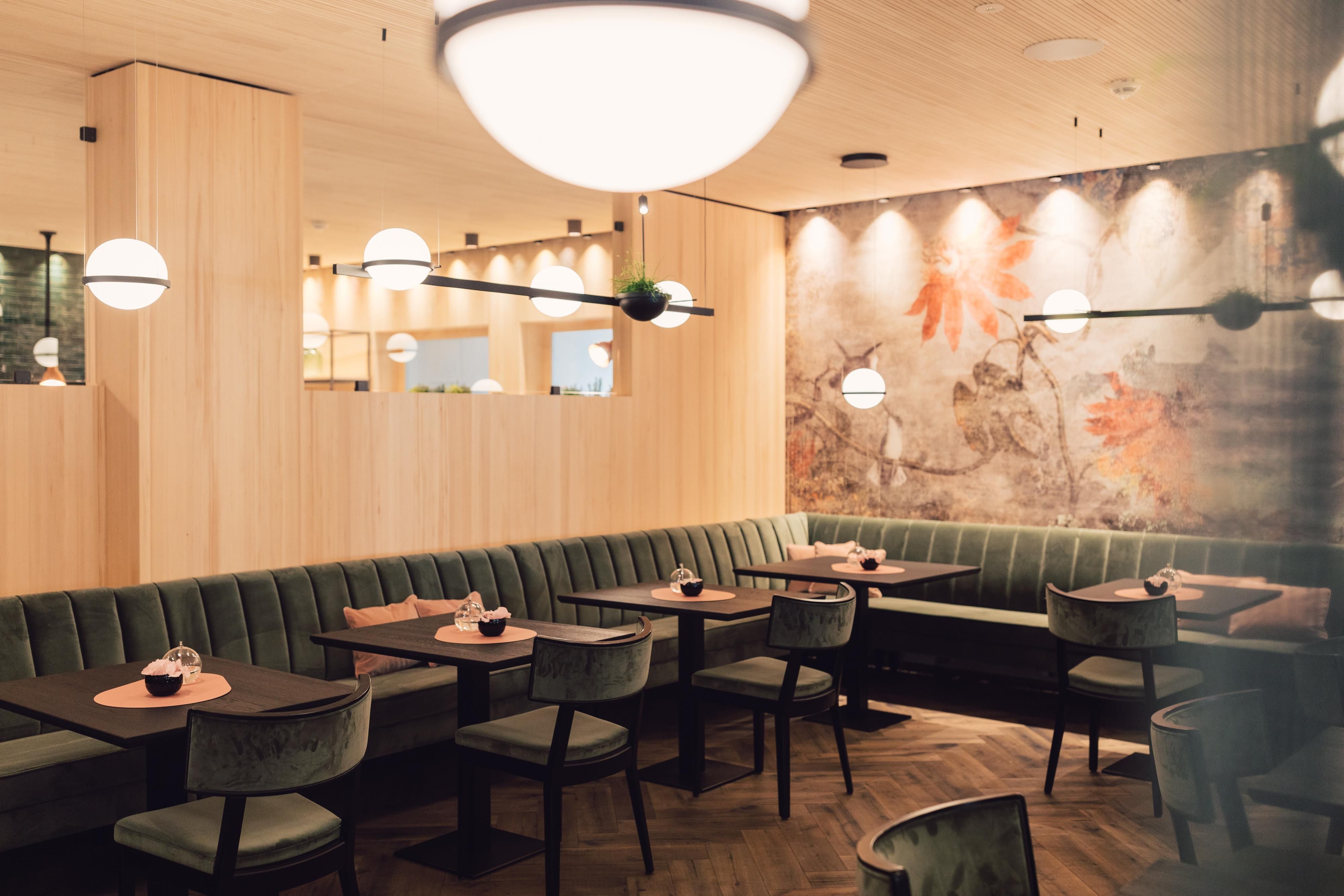 A modern restaurant with elegant wood paneling and stylish lamps. The cozy tables are surrounded by a green seating area, creating an inviting atmosphere.