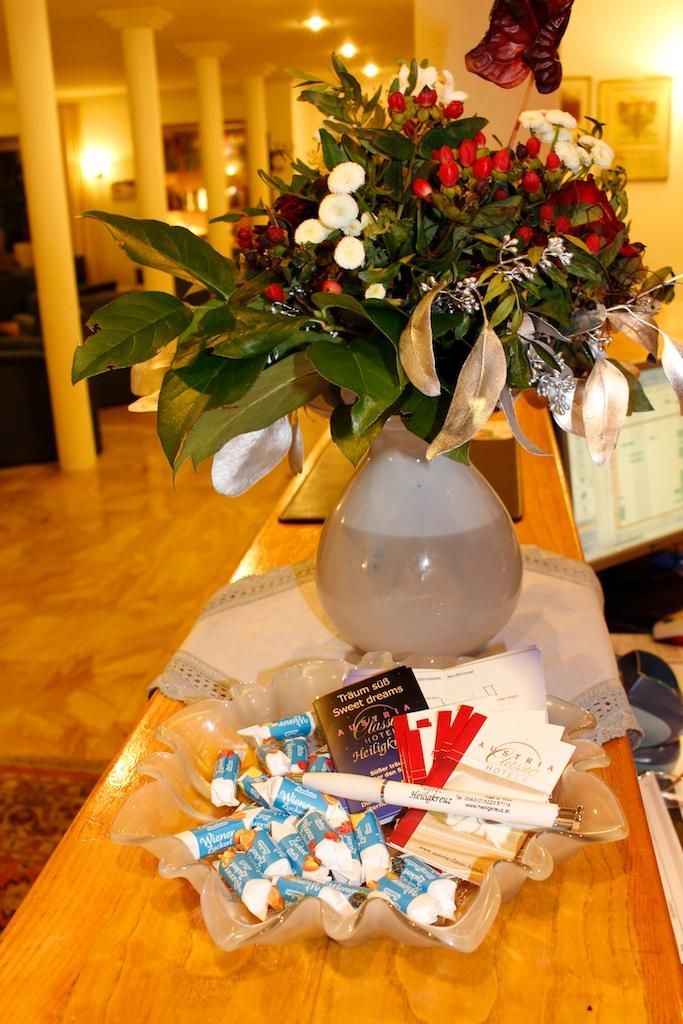 A beautiful bouquet of flowers in a vase is on a table. Next to it lies a bowl with various small items and cards.