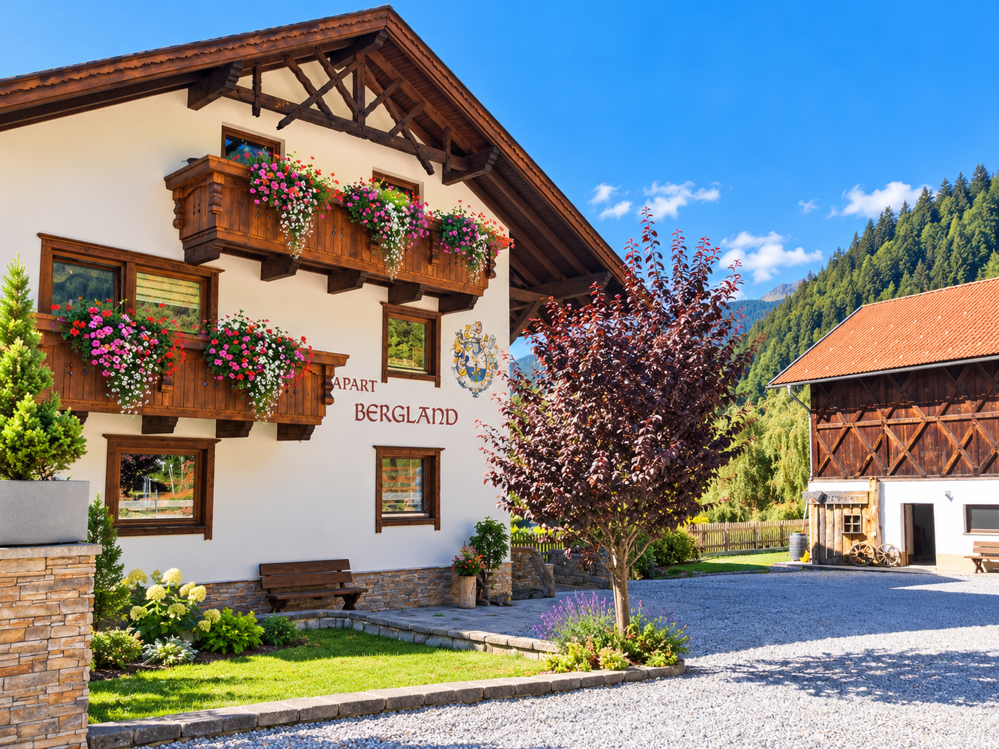 A charming apartment building with blooming balconies and an inviting landscape. In the background, wooded mountains can be seen.