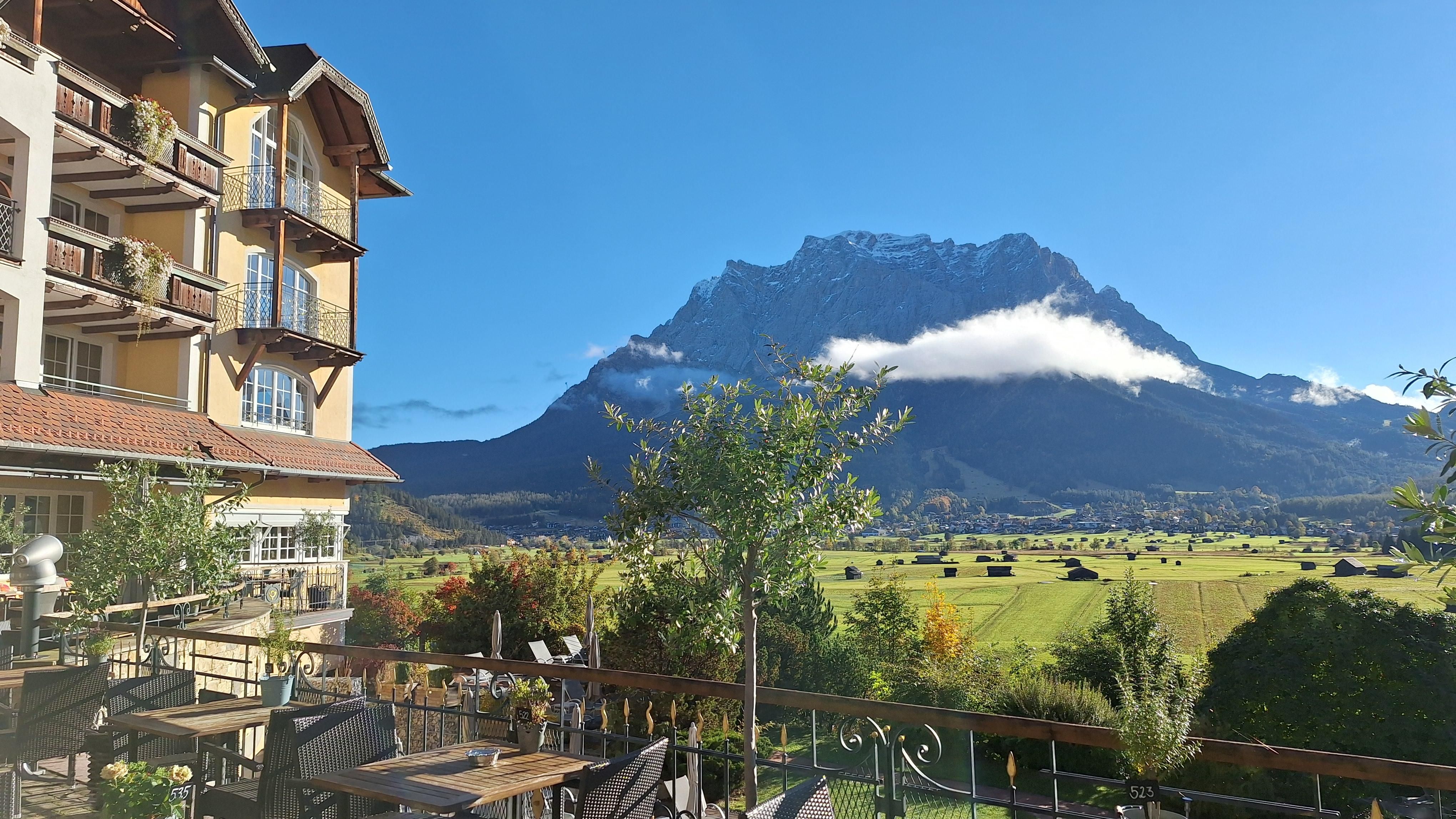 A picturesque landscape with an impressive mountain in the background. In the foreground, several tables on a terrace and green meadows can be seen.
