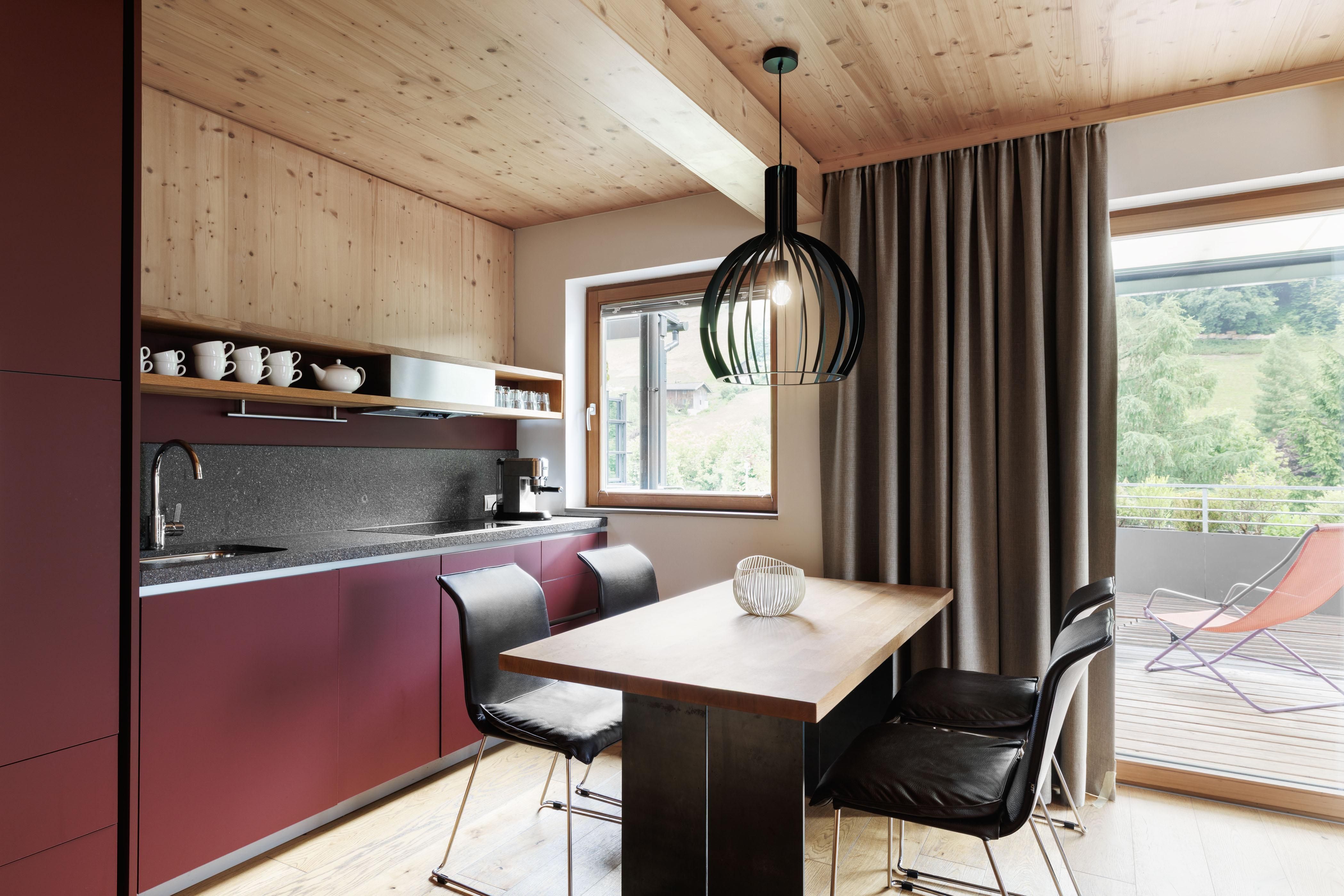 A modern kitchen with wood details and a large window. The table is made of wood and the chairs are black.