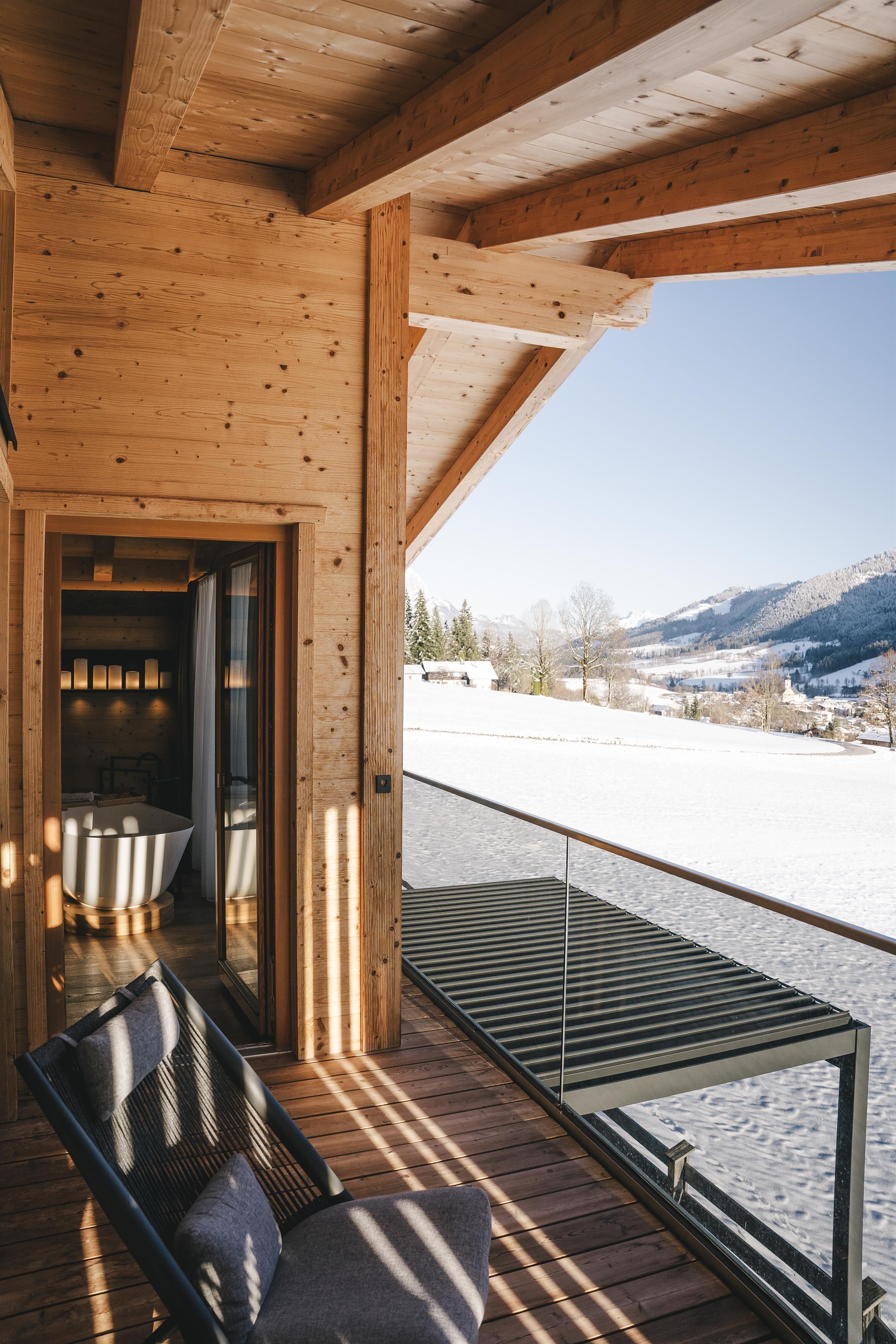 A modern wooden terrace with a view of snow-covered mountains. The decor is cozy and inviting.