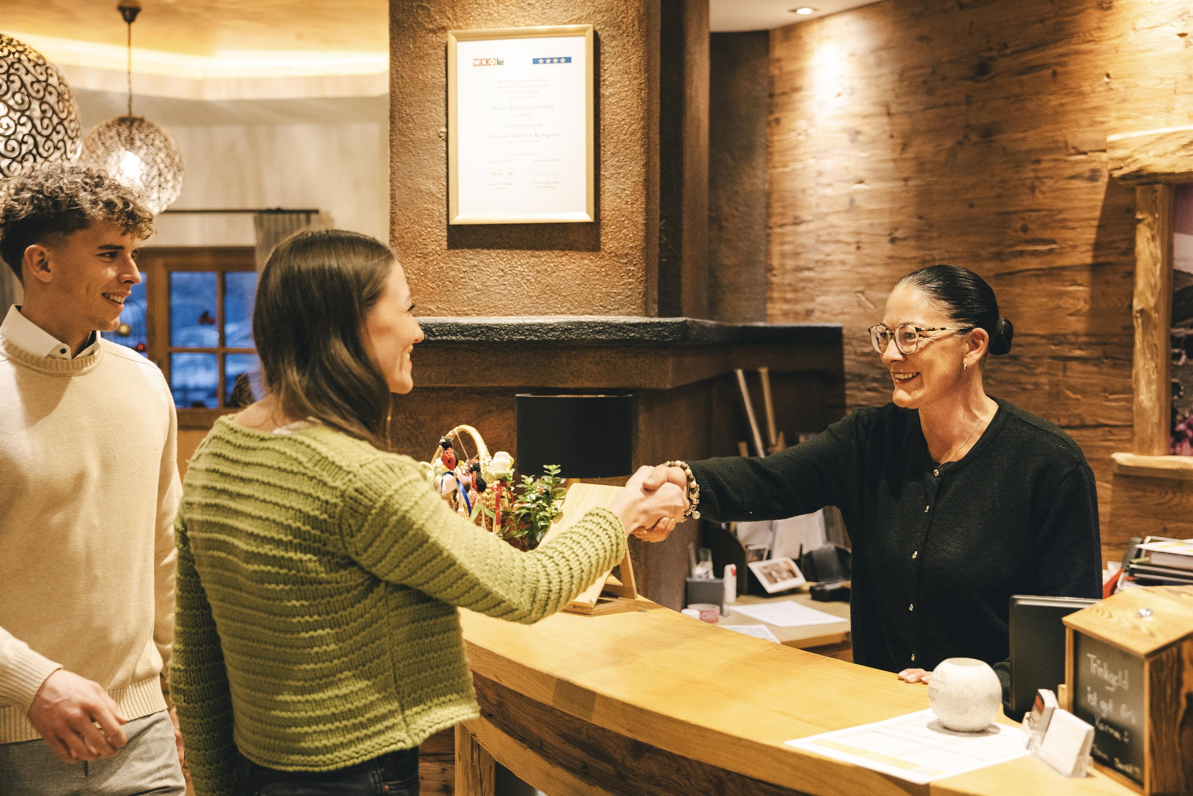 A friendly greeting at the reception. A woman shakes hands with the reception lady, while a young man watches.