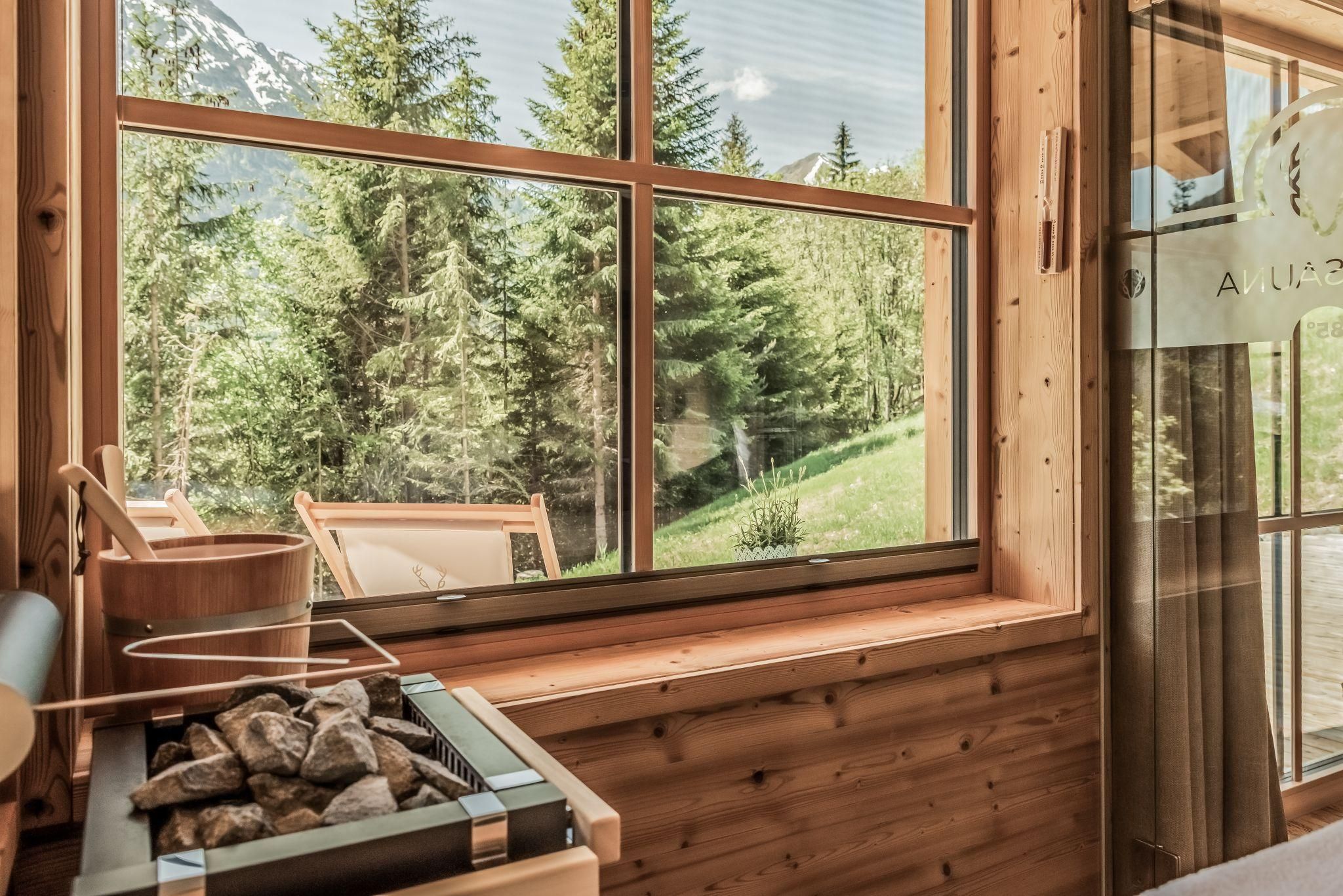 A cozy room with large windows that offer a view of green trees and nature. In the foreground, there is a small fire pit.