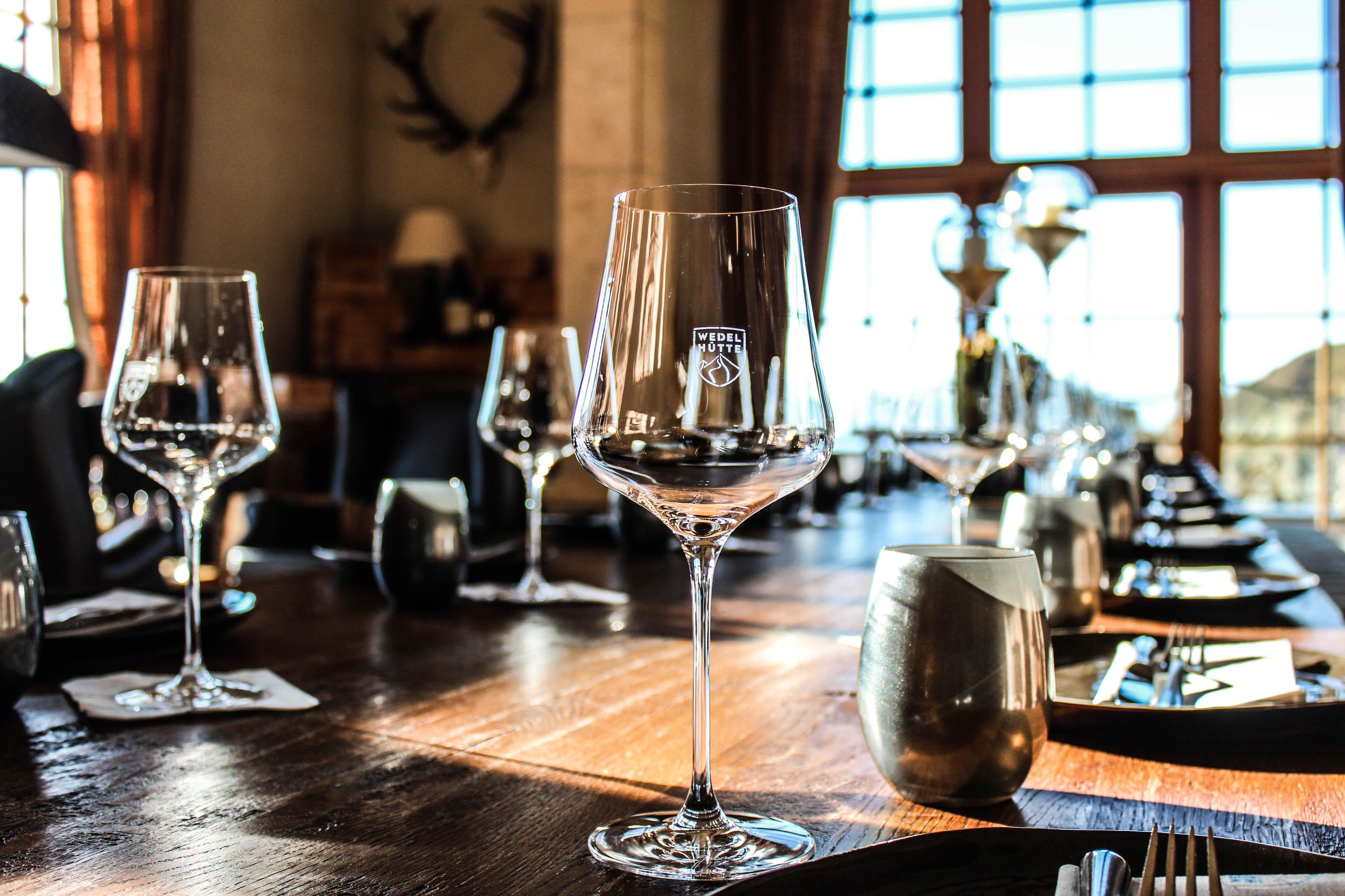 An elegant table in a stylish restaurant, set with glasses and cutlery. Large windows let in daylight and create an inviting atmosphere.