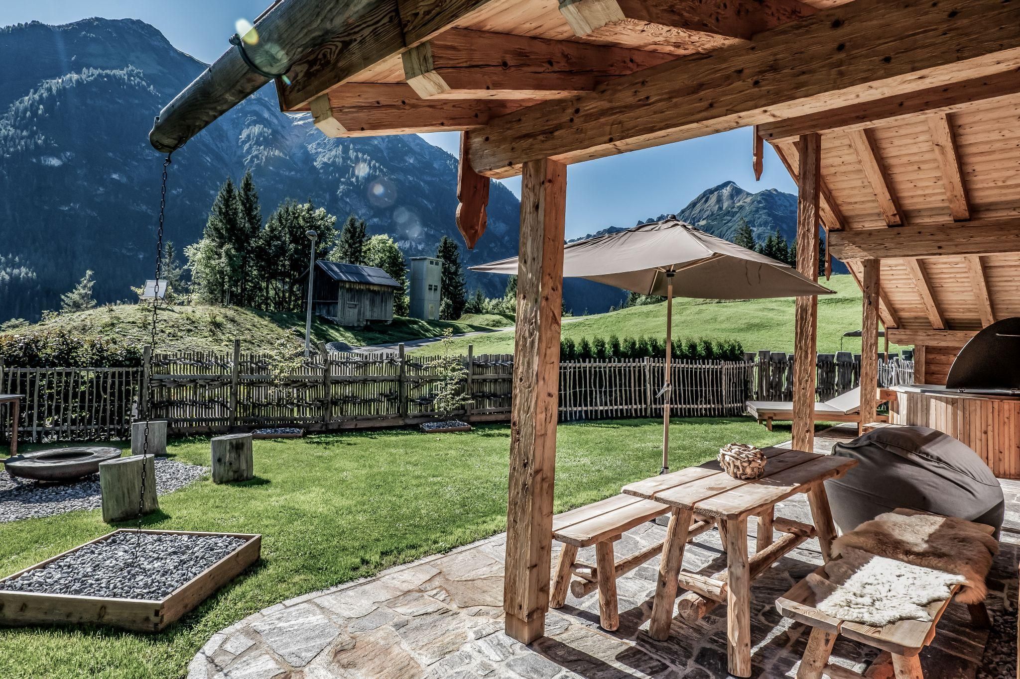 A cozy outdoor area with a wooden table and benches. In the background, green meadows and mountains can be seen.