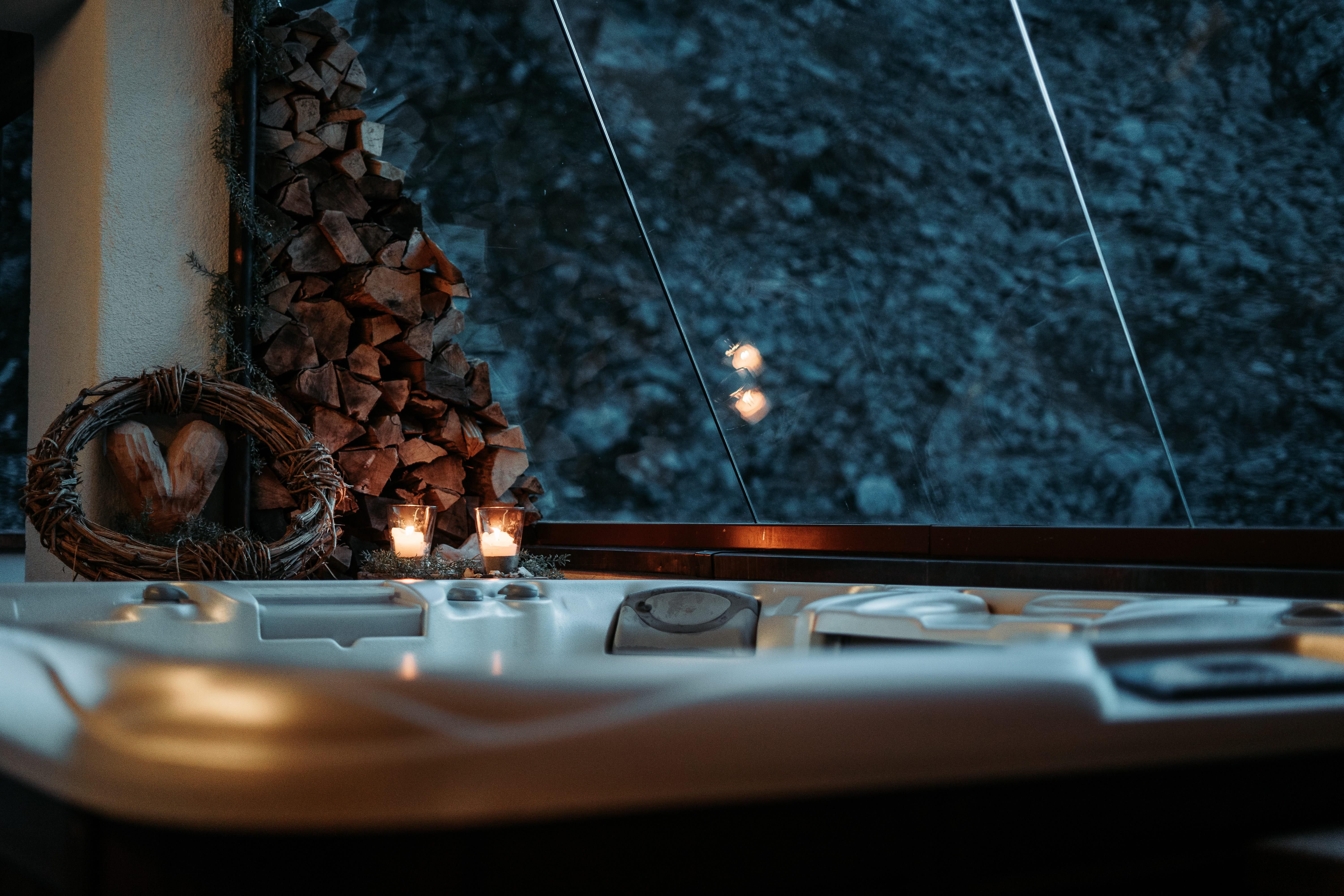 A stylish hot tub in a modern room with wooden decor and candles. In the background, a rocky wall is visible, creating a cozy atmosphere.
