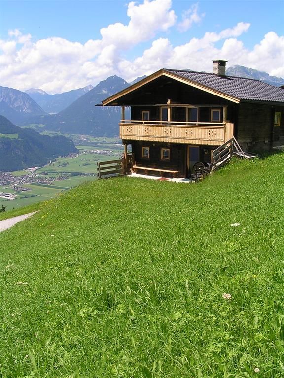 A cozy wooden house on a green meadow with a view of the mountains. The sky is clear and it is sunny.