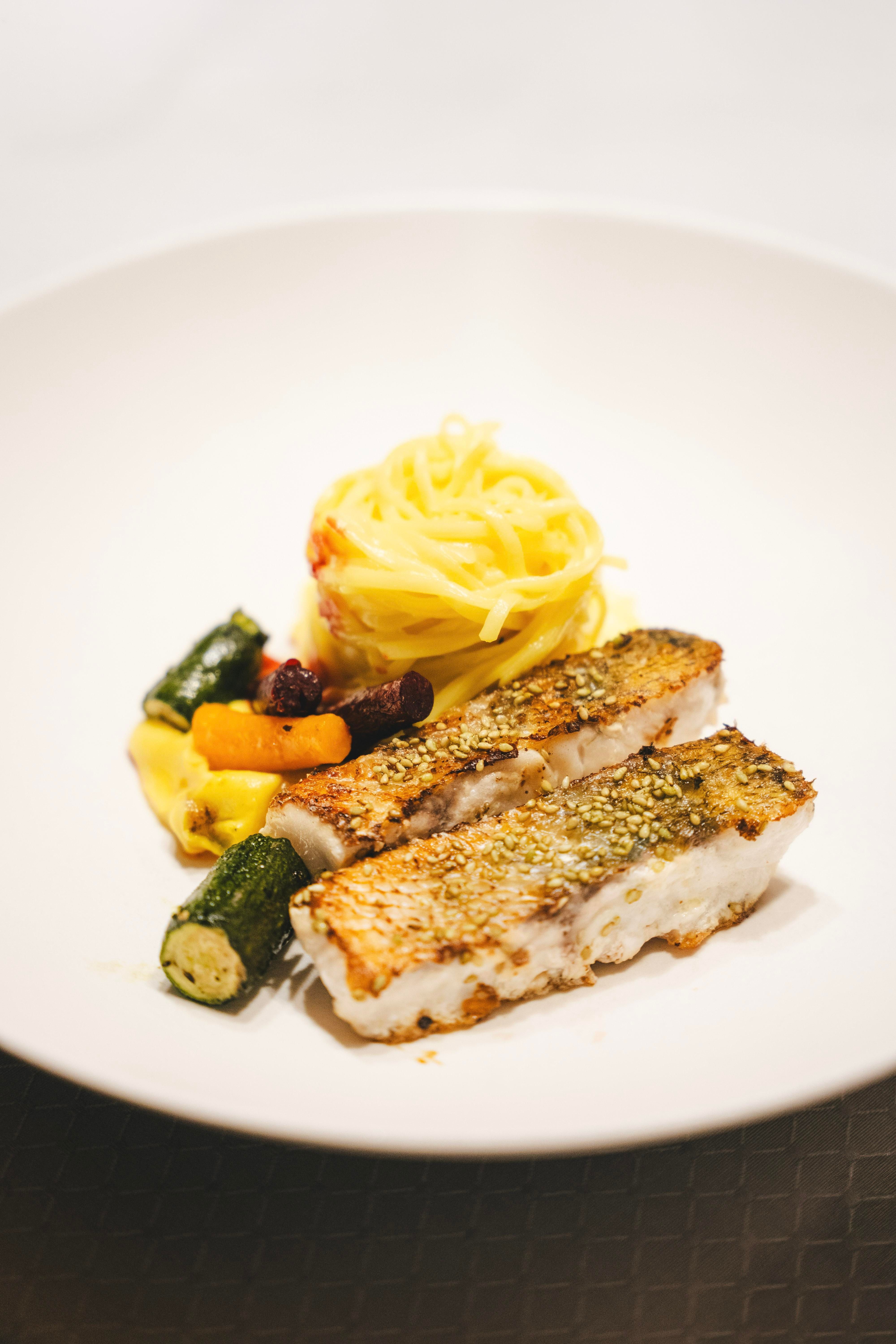 A plate with fried fish, served with pasta and colorful vegetables. The dish looks appetizing and fresh.