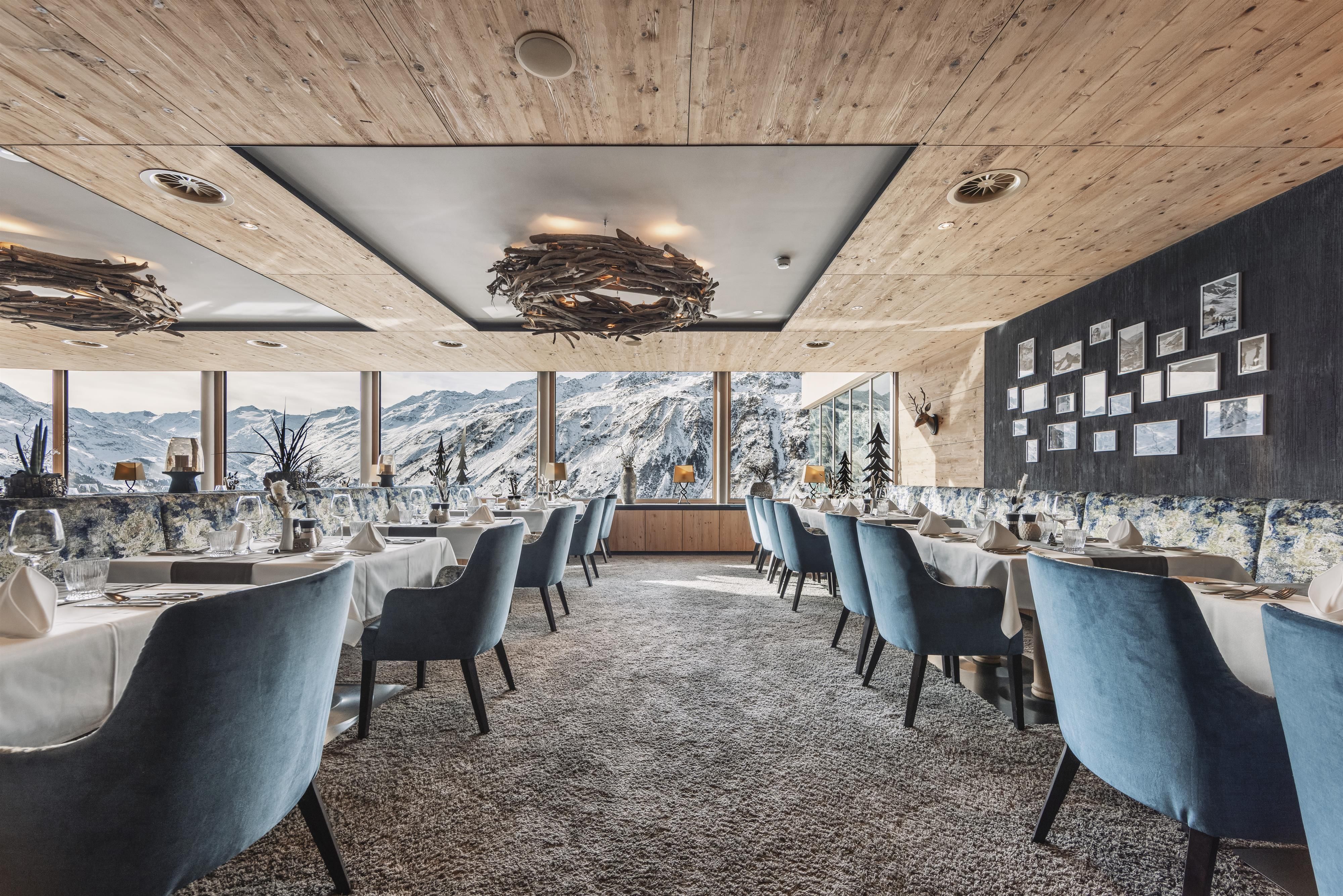An elegant restaurant with blue chairs and large windows that offer a view of the mountains. The interior is modern and cozily furnished.