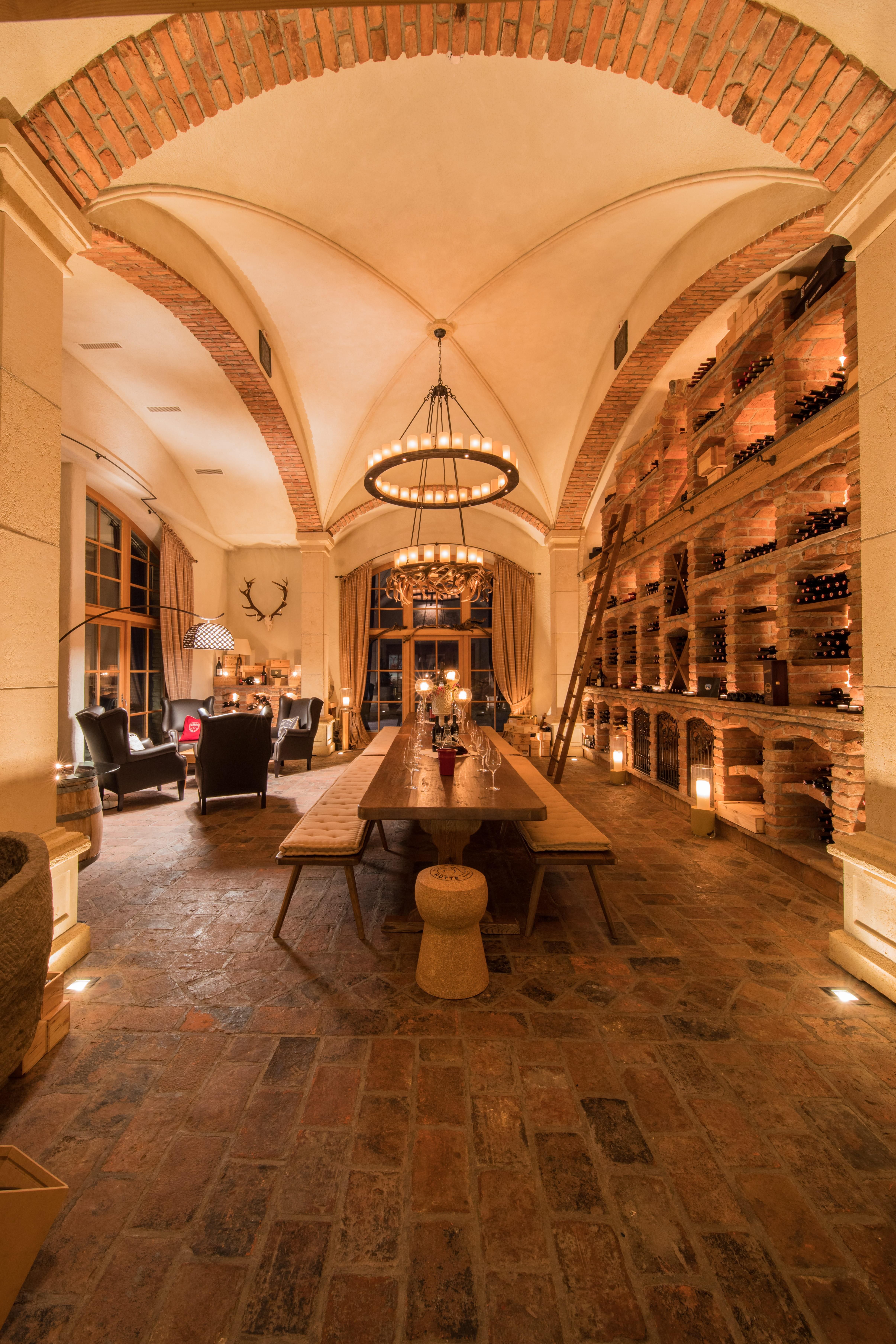 A stylish wine cellar with a long wooden table and cozy seating. The ceiling is designed with bricks and the walls are decorated with wine shelves.