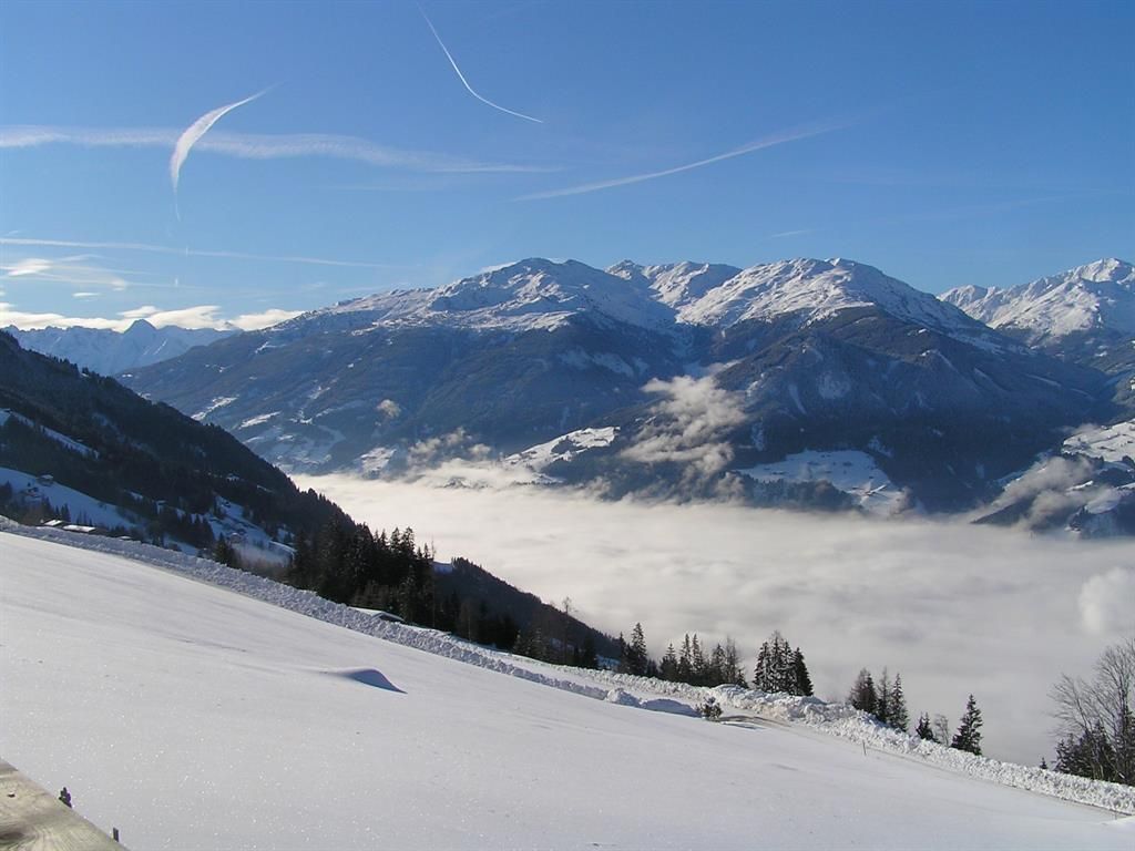 A beautiful mountain landscape with snow-covered peaks and a clear blue sky. In the valley, dense clouds lie.