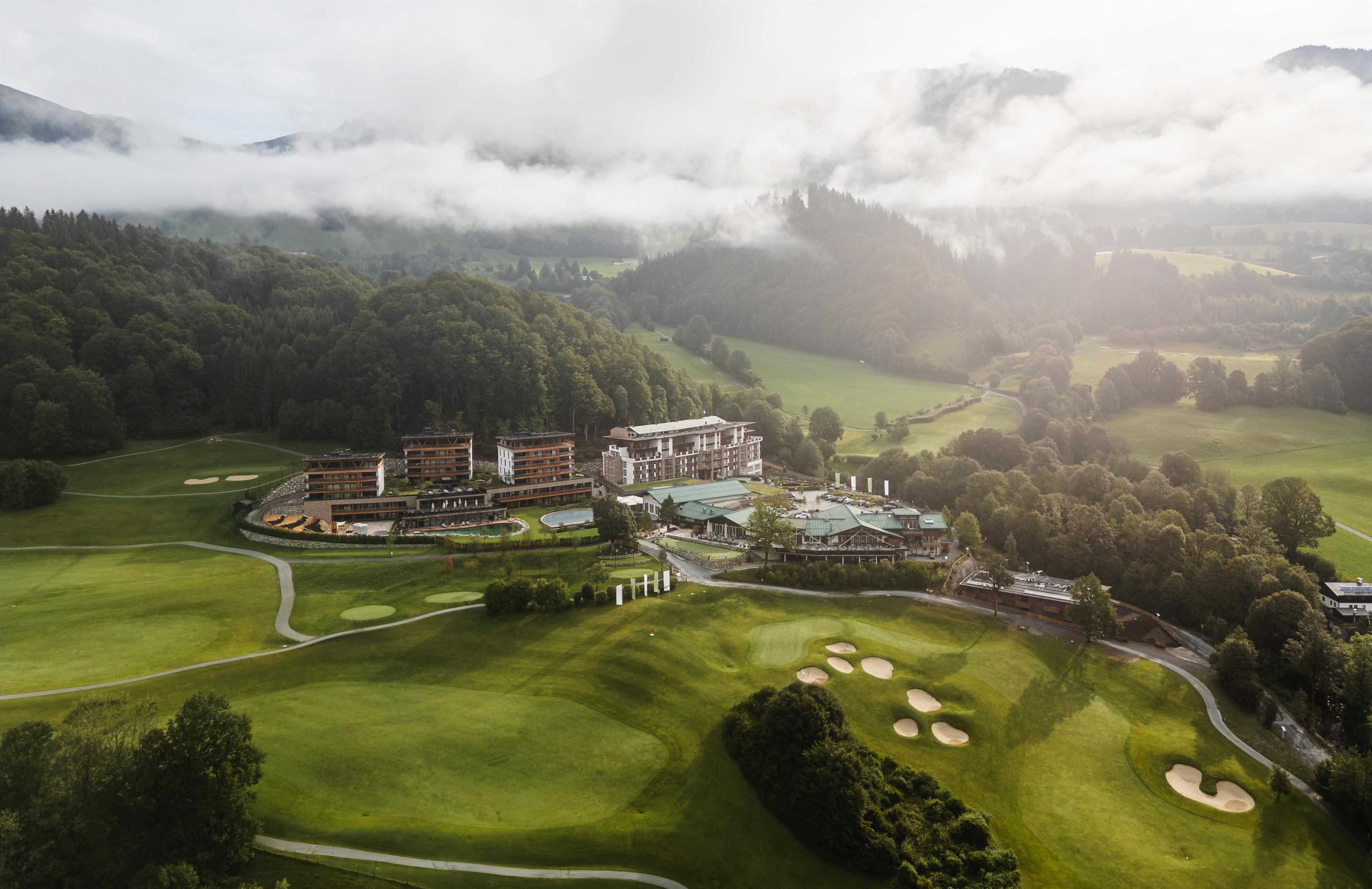 A picturesque golf resort in a green landscape with gentle hills. The sky is overcast, and the surroundings exude tranquility.