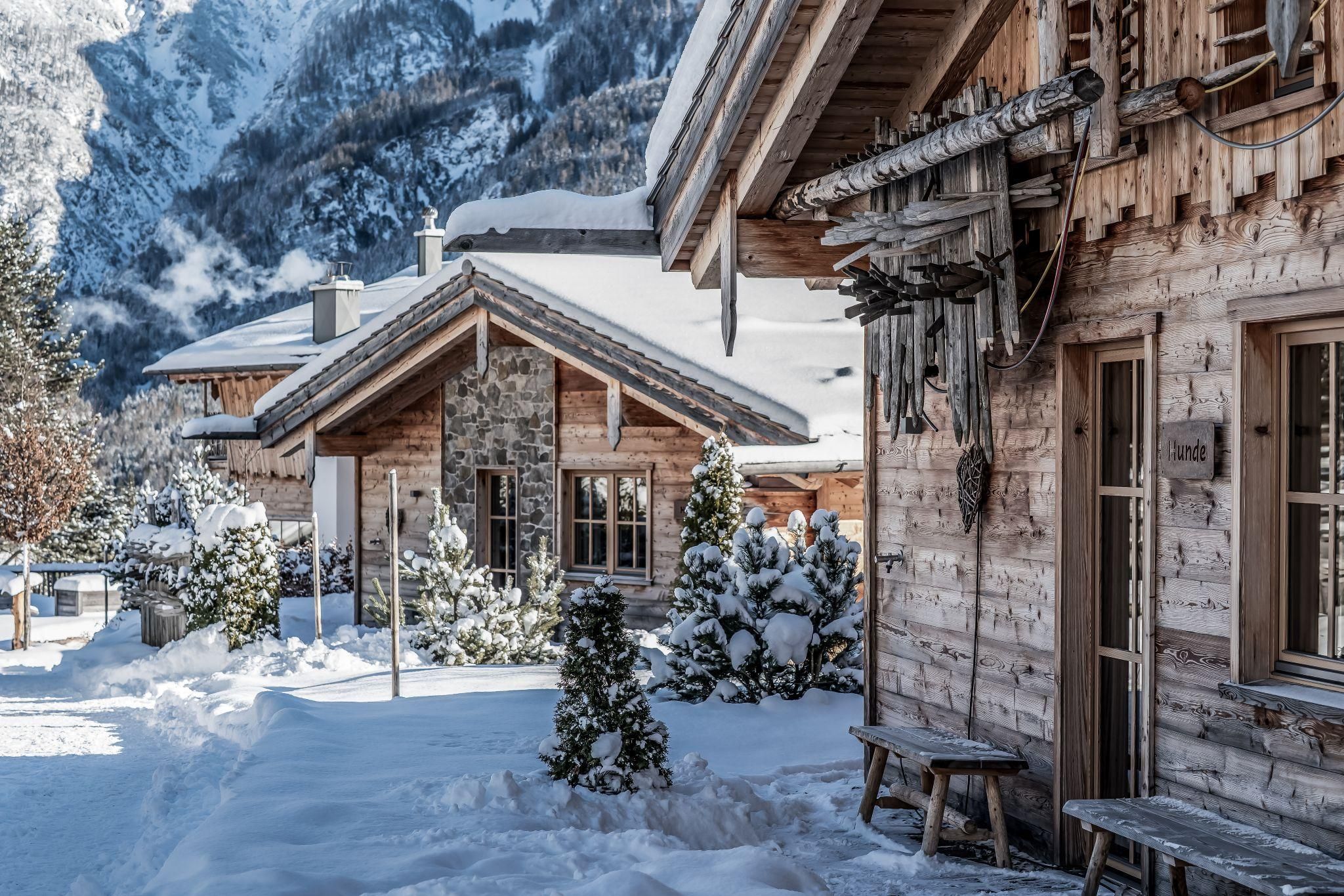 A group of chalets in a snowy landscape. The surroundings are peaceful and picturesque, surrounded by mountains and fir trees.