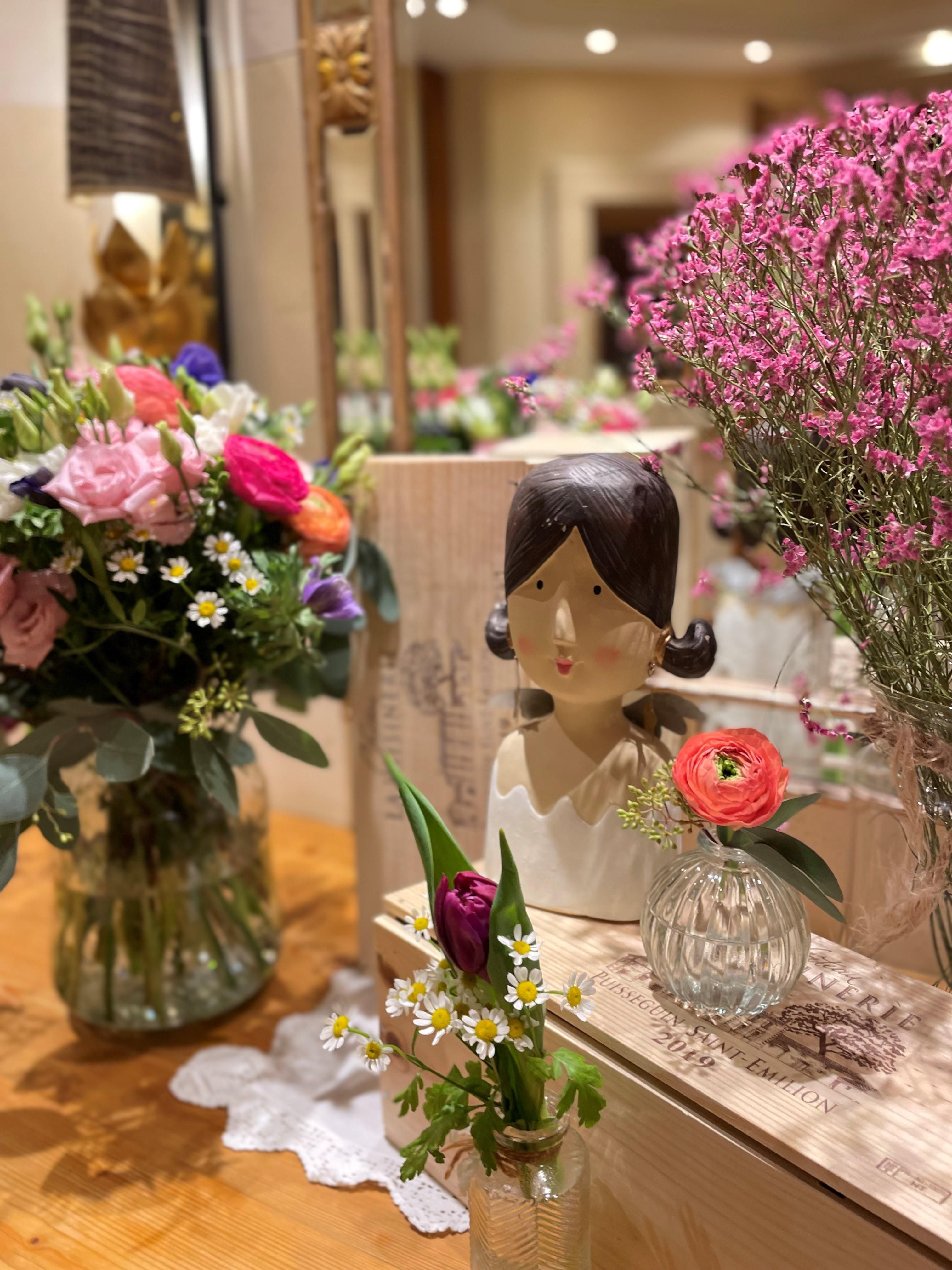 A beautiful arrangement with a flower container and a decorative statue. On the table, various flowers and plants are visible in clear vases.