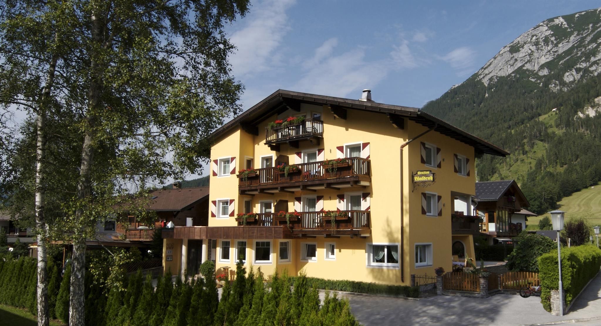 A cozy yellow building with balconies and beautiful windows. In the background, mountains and green grass are visible.