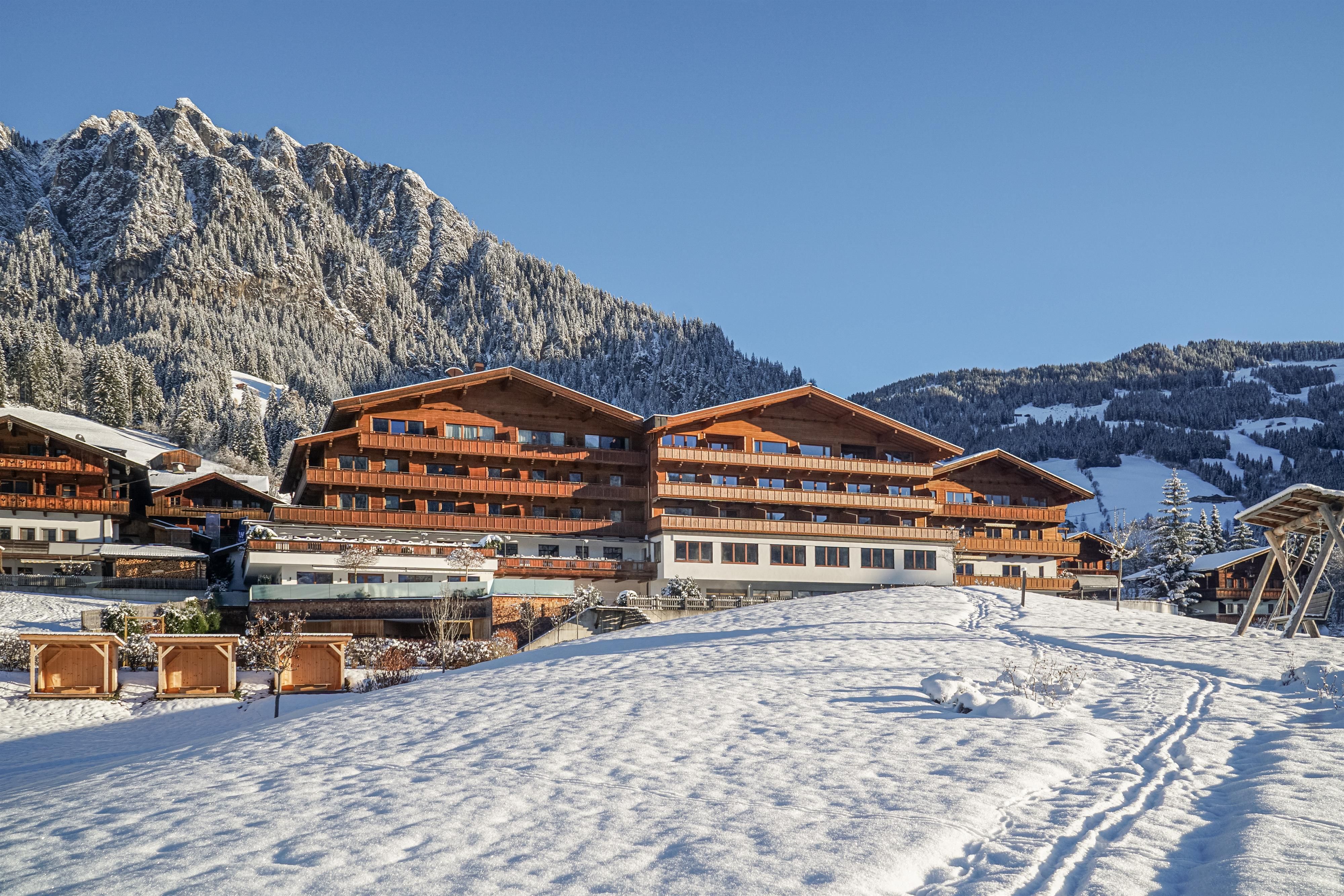 A traditional wooden building in a snowy mountain landscape. In the background, there are high mountains and a blue sky visible.