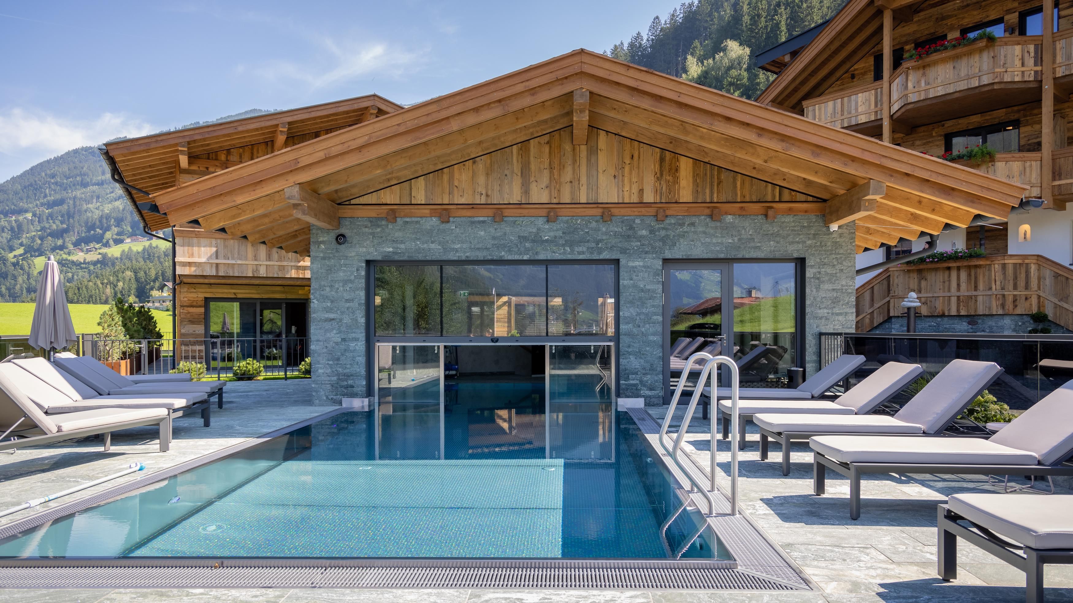 A modern wellness area with a pool and loungers. The background features a mountain landscape under a clear sky.