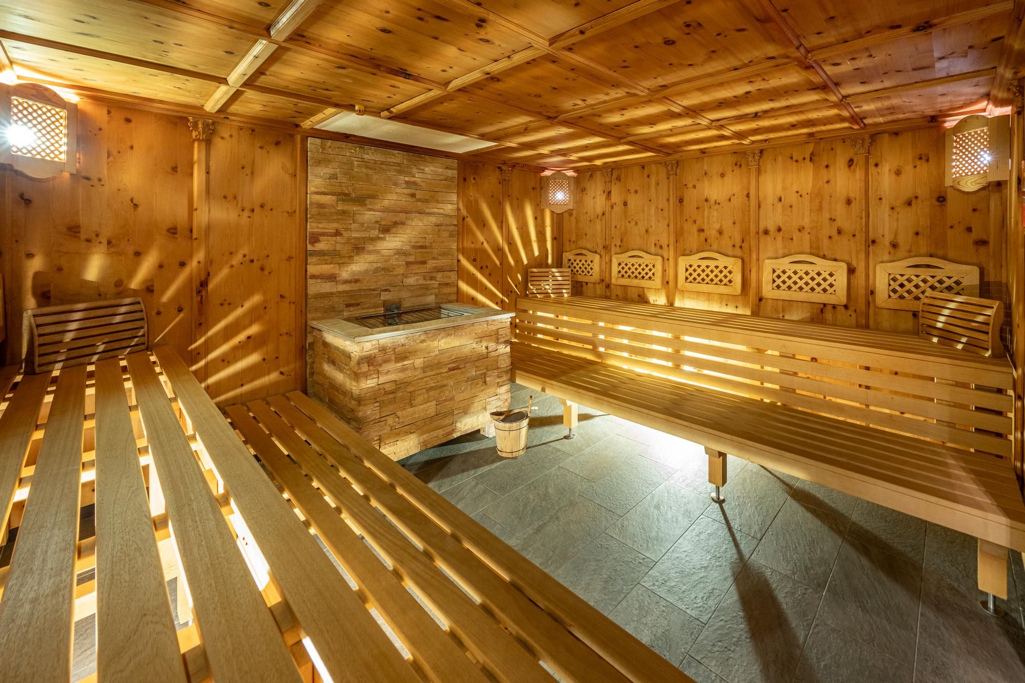 A cozy pine sauna with wooden lounging areas and soft lighting. The room exudes peace and relaxation.